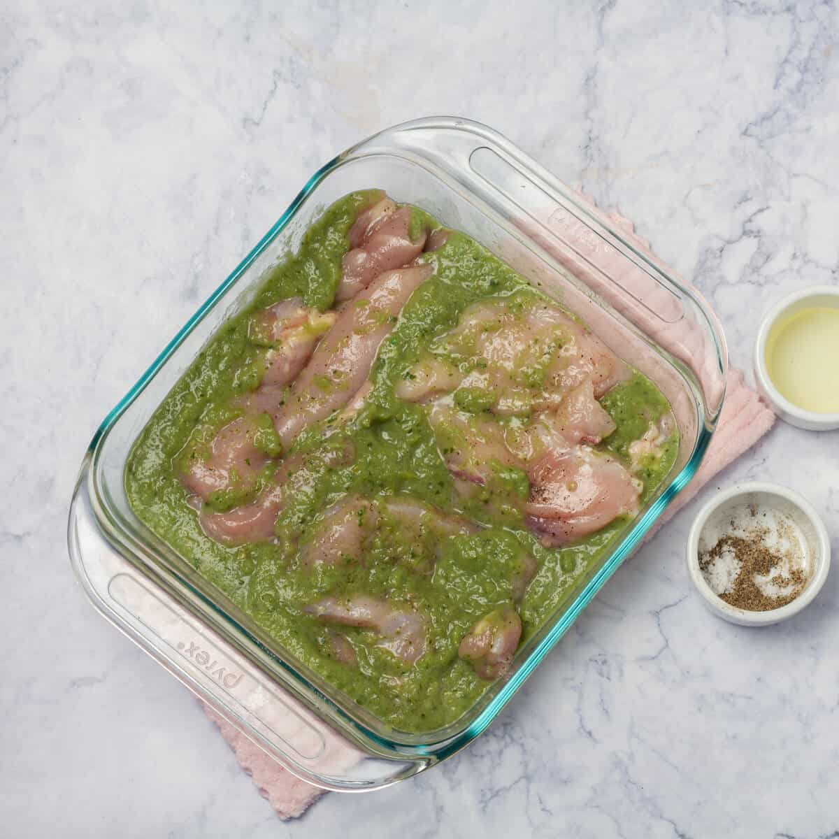Seasoned chicken marinating in salsa verde sauce in a baking dish. 