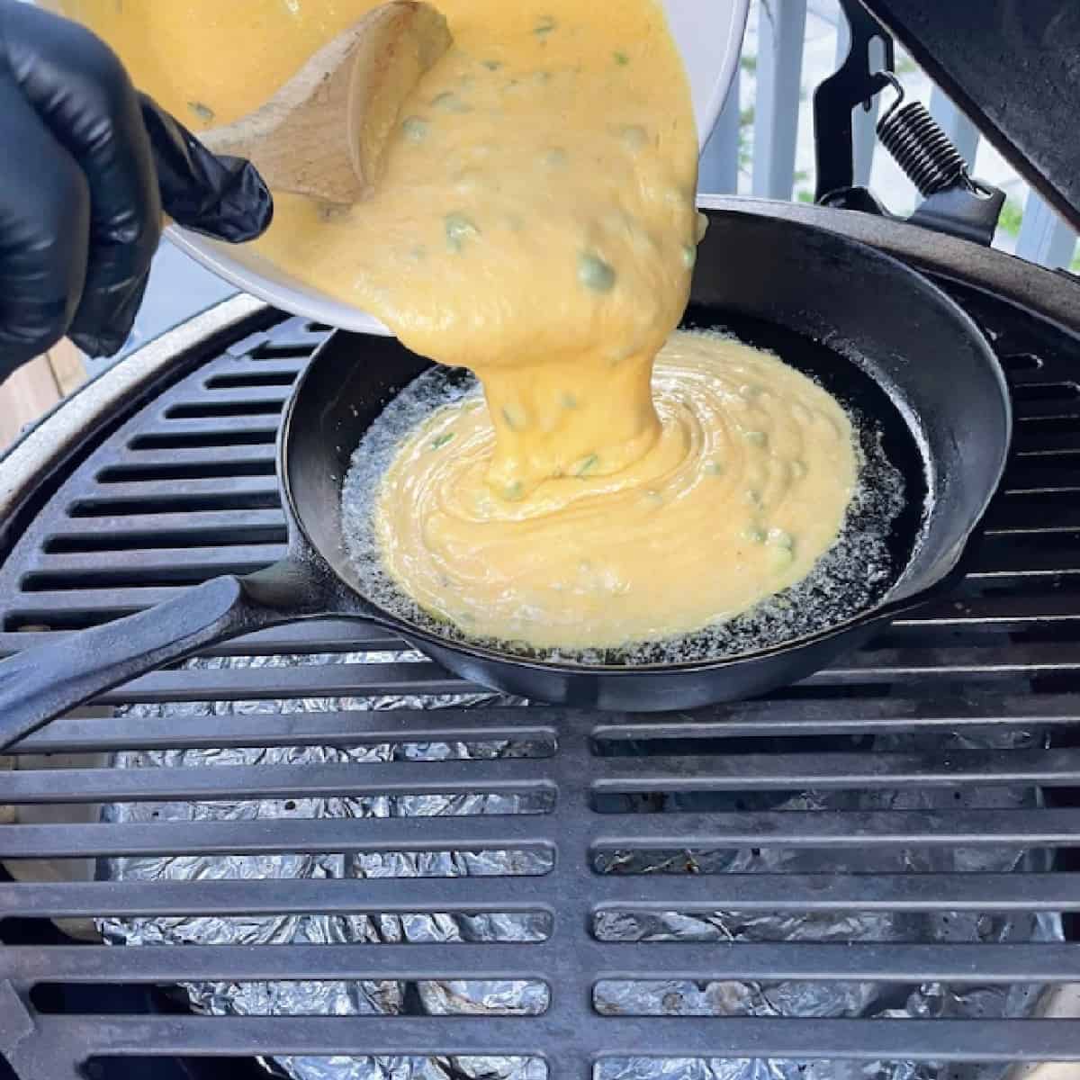 jalapeno cornbread mix being pouring into cast iron skillet on grill