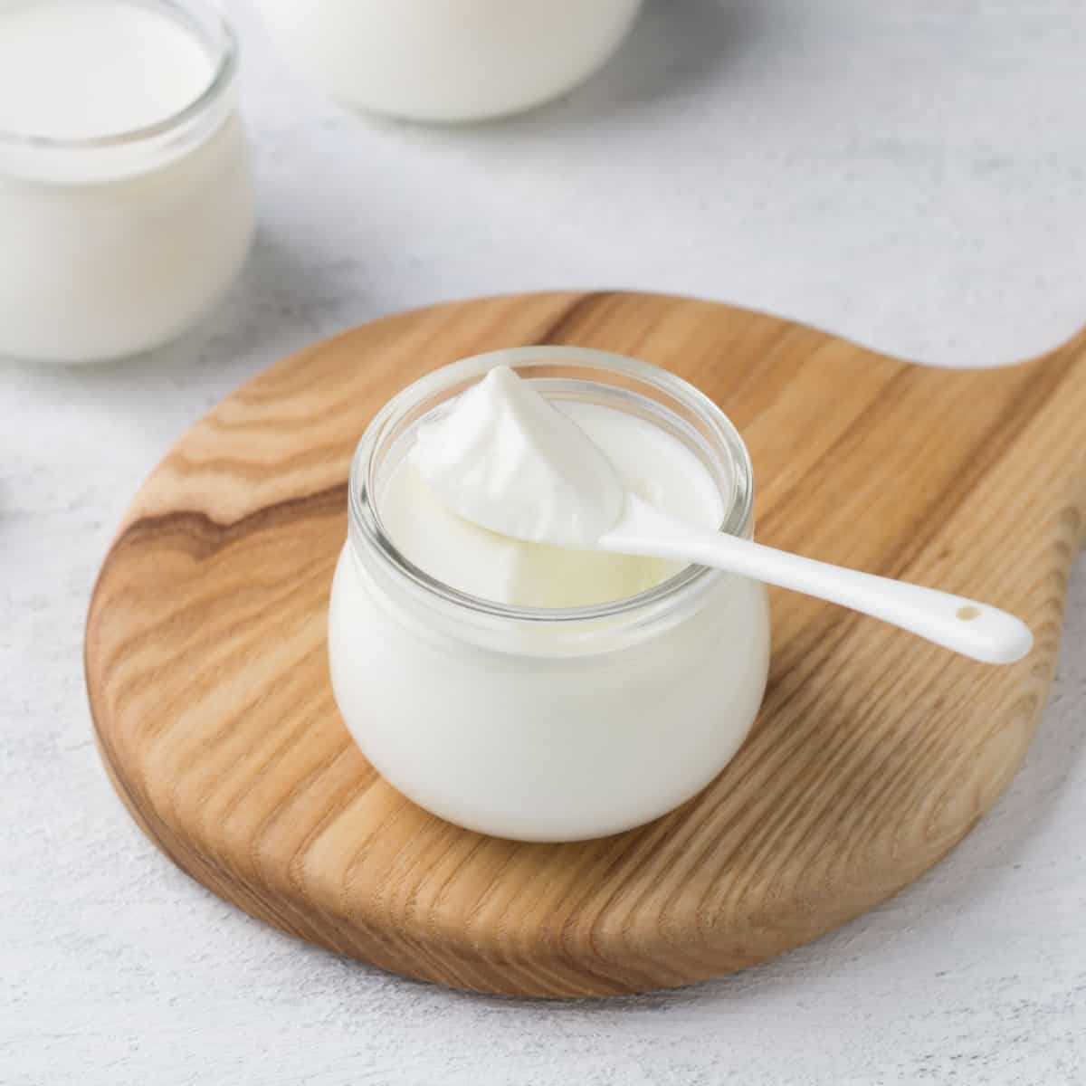 Greek yogurt in jar on wooden cutting board