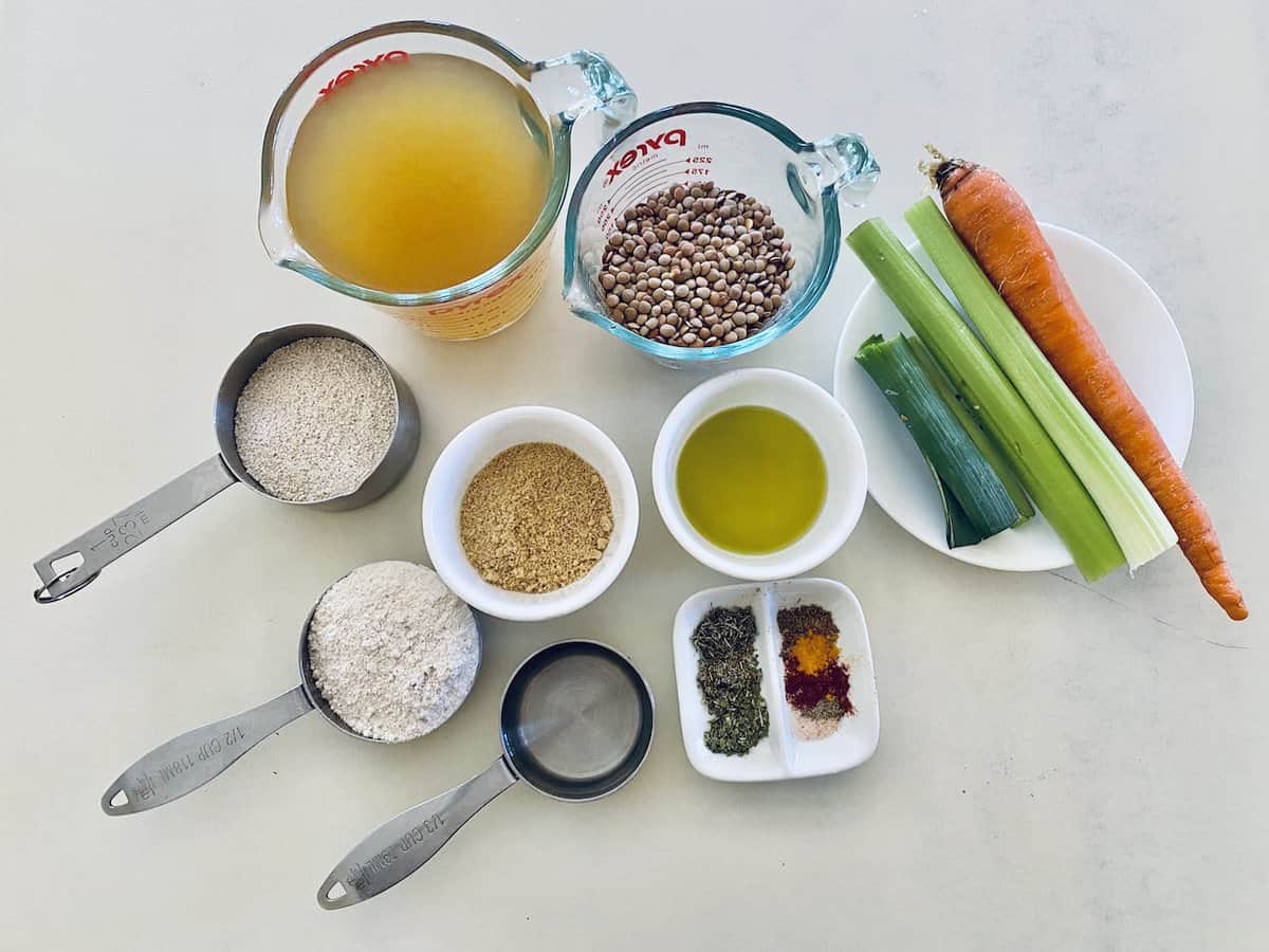 Lentil loaf ingredients of uncooked lentils, vegetable broth, flax meal, water, oats, oat flour, a carrot, celery, leek, oil, and seasonings, in separate dishes.