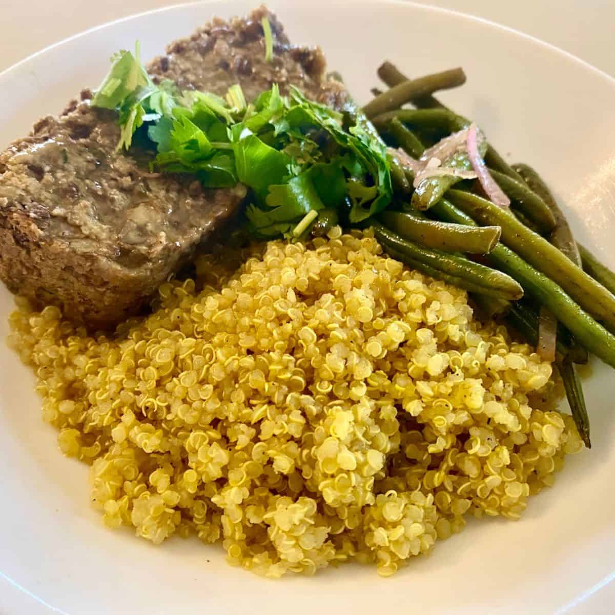 Hearty and flavorful Vegan Lentil Loaf on a plate with green beans and quinoa.