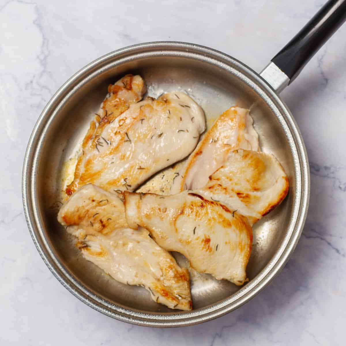 Grilling seasoned chicken breasts in a pan. 