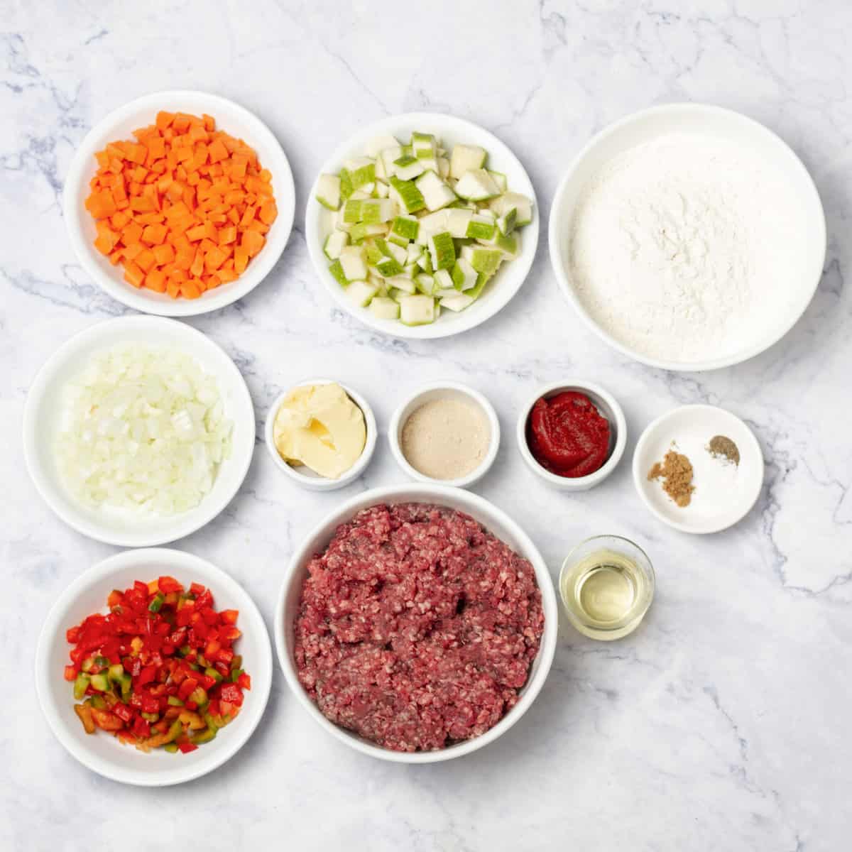 Beef Pie ingredients of flour, yeast, butter, vegetables, ground beef, tomato paste, and seasonings in separate dishes. 