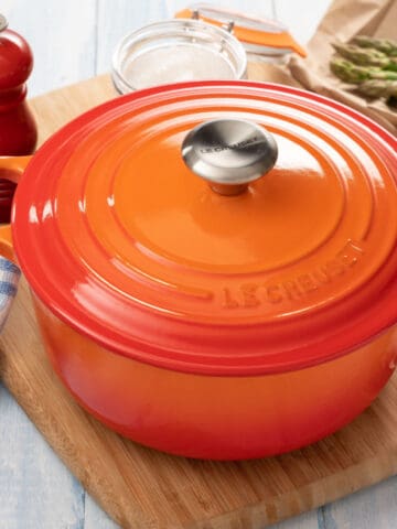 orange le creuset dutch oven sitting on wooden cutting board