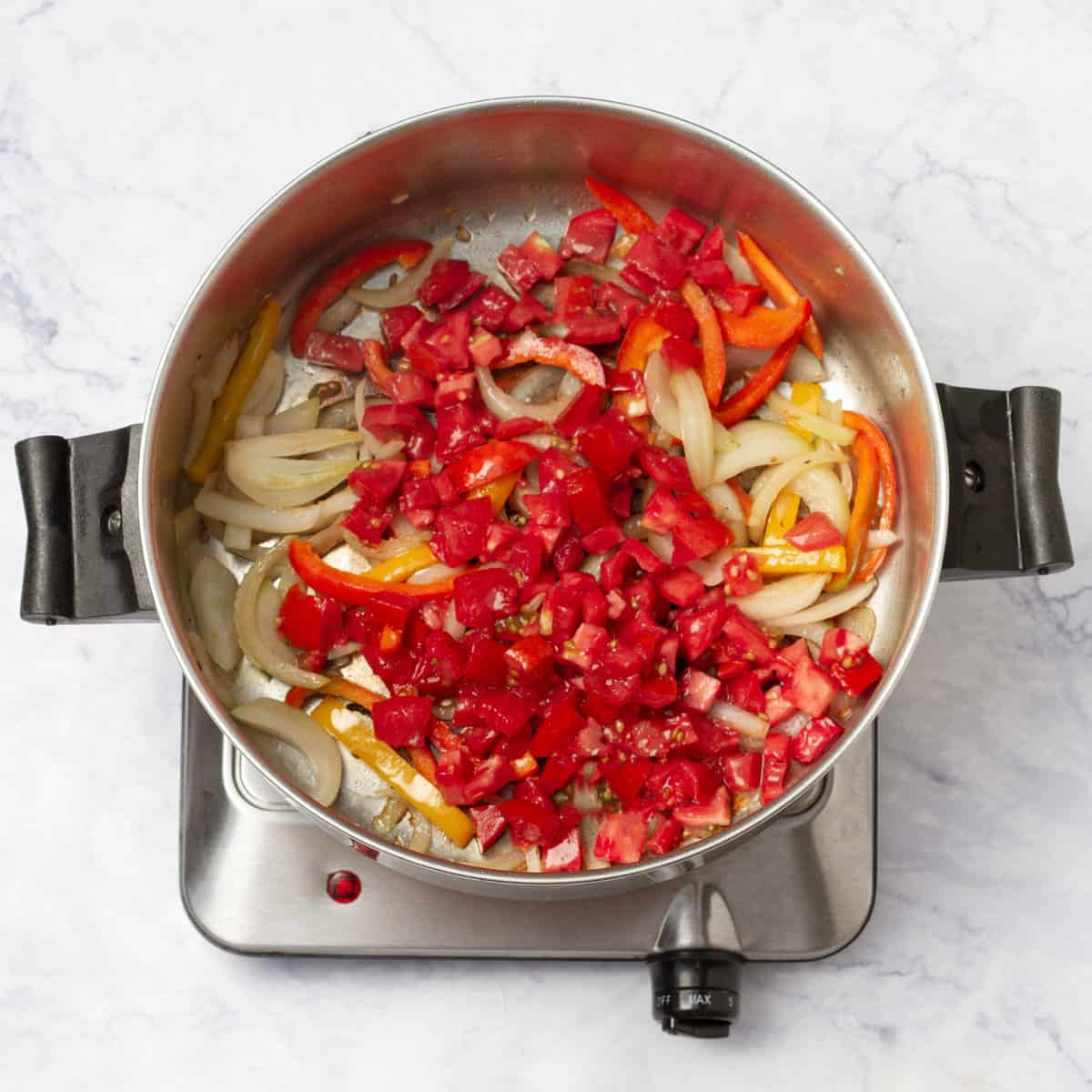 Sliced onions, red and yellow bell peppers, and diced tomatoes in a saucepan