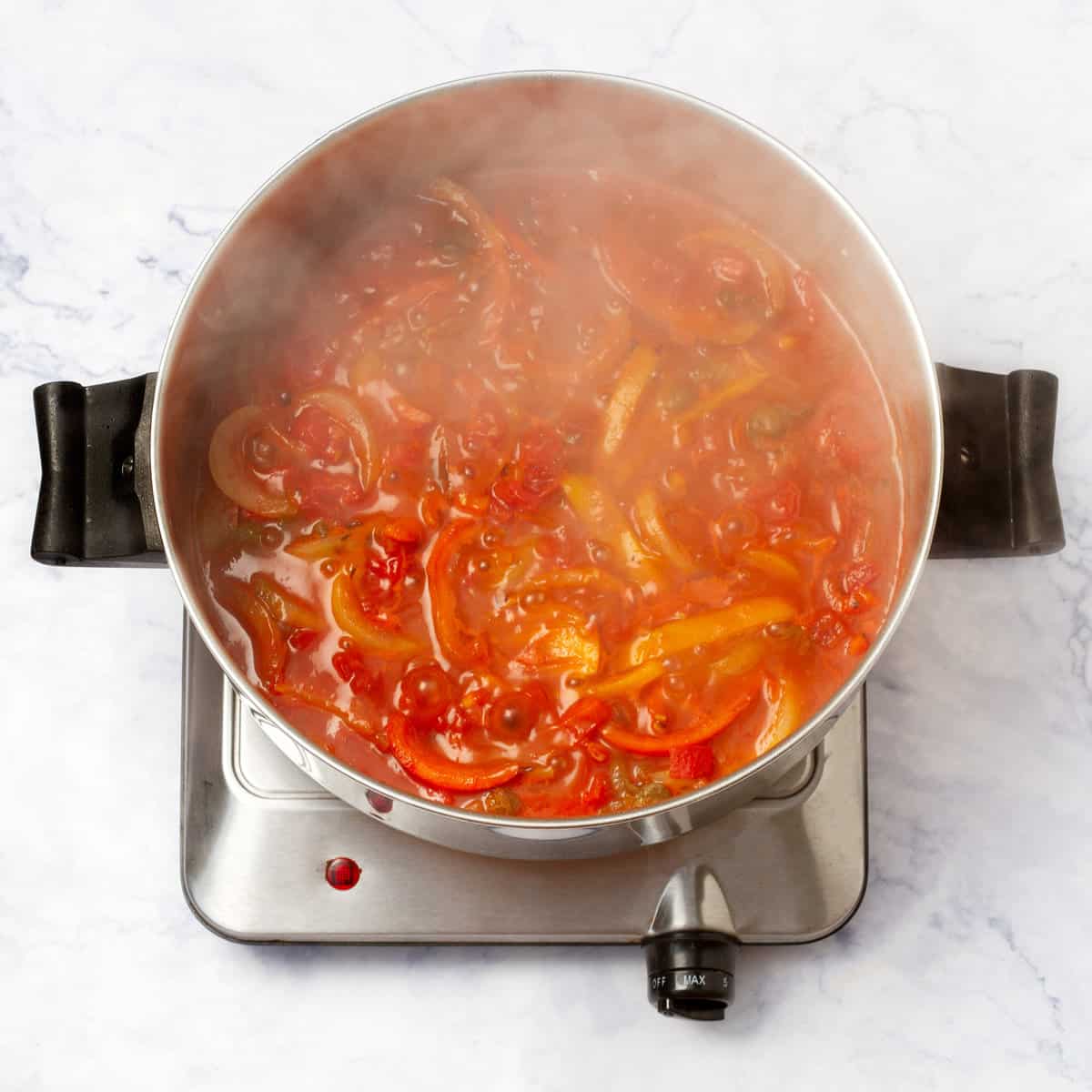 Sliced onions, red and yellow bell peppers, and diced tomatoes cooking in a saucepan