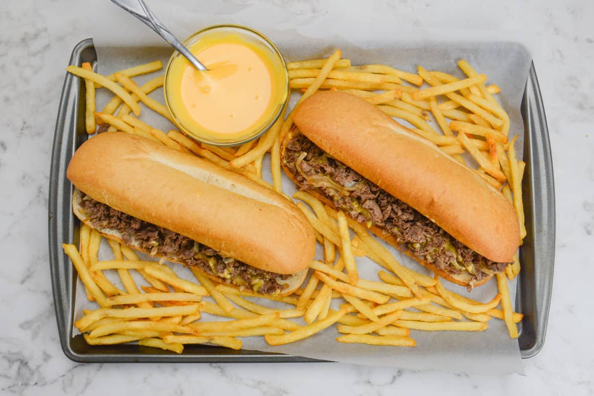 blackstone philly cheesesteaks on tray with french fries and cheese sauce.