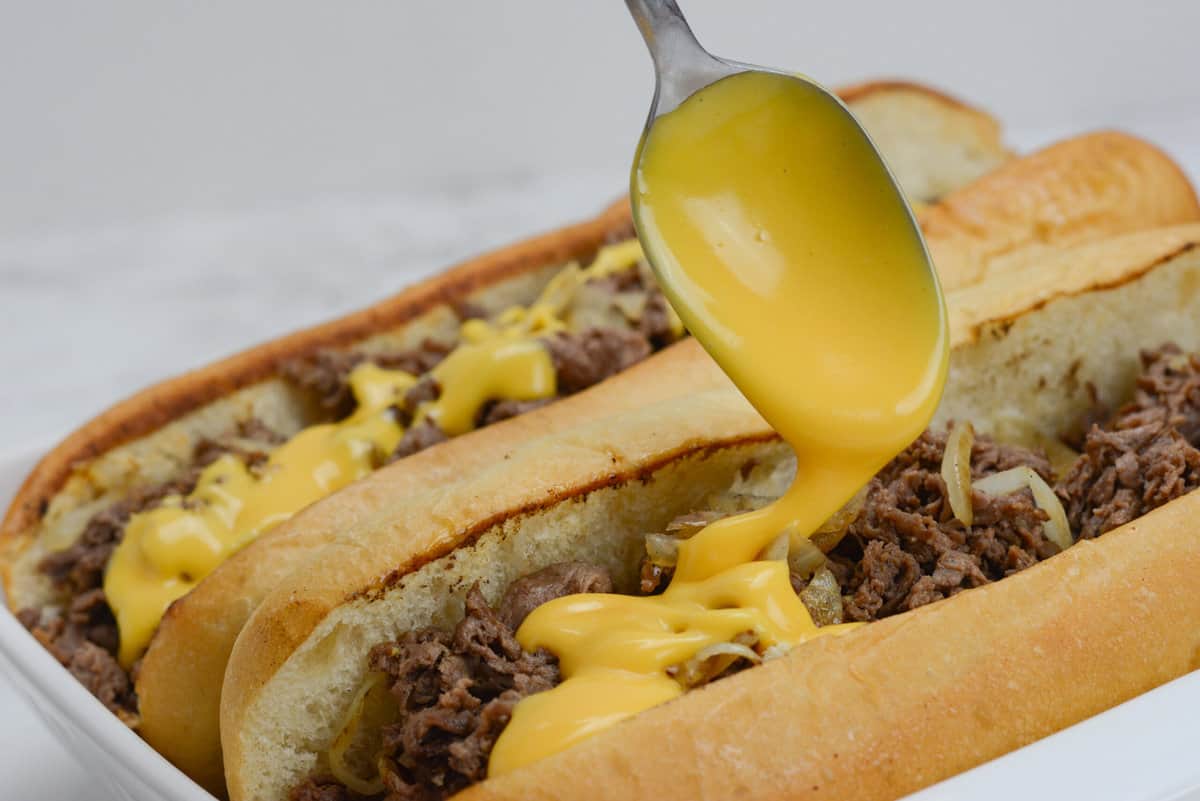 drizzling cheez whiz on blackstone philly cheesesteaks.