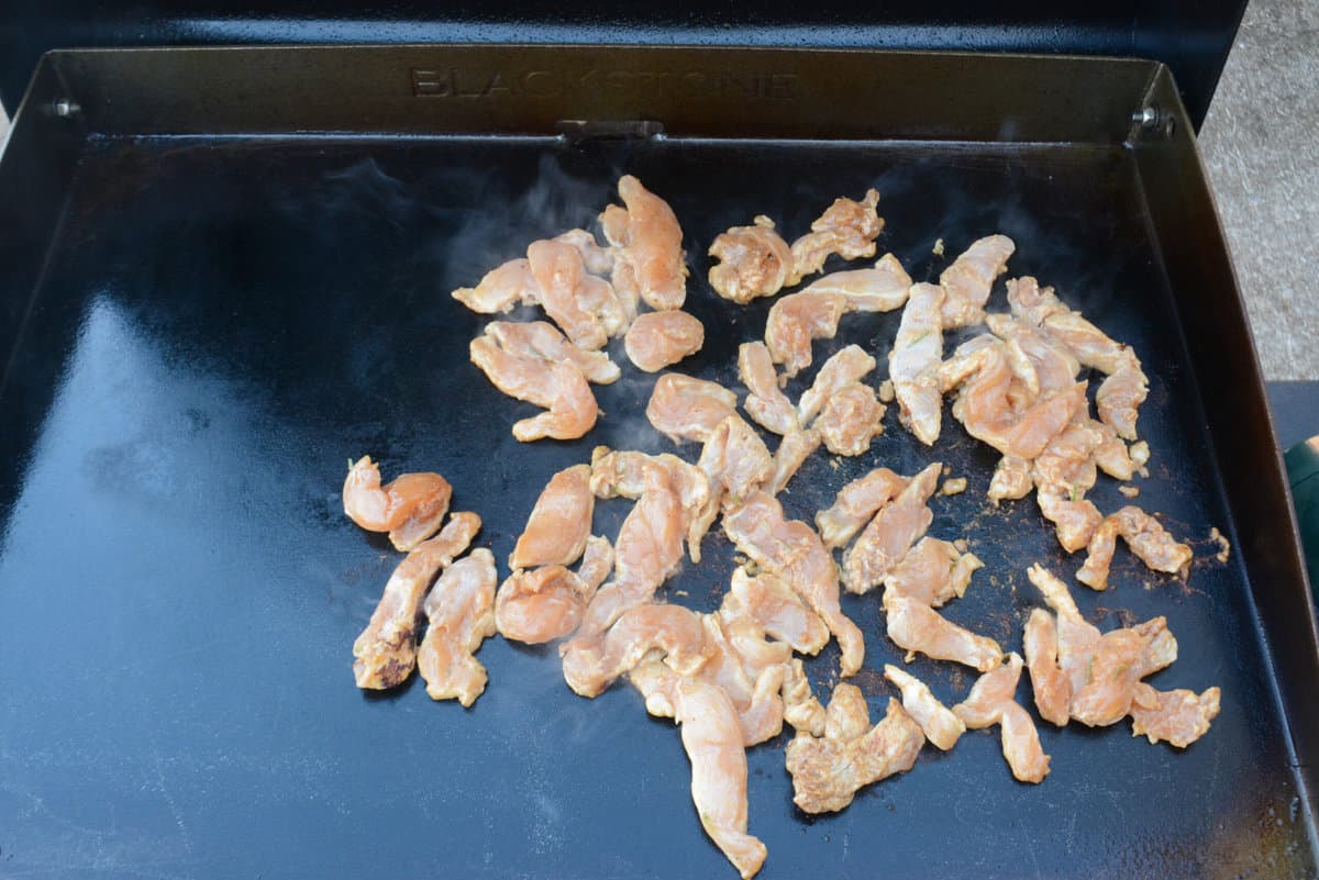The seasoned chicken strips are placed on top the oiled Blackstone griddle 
