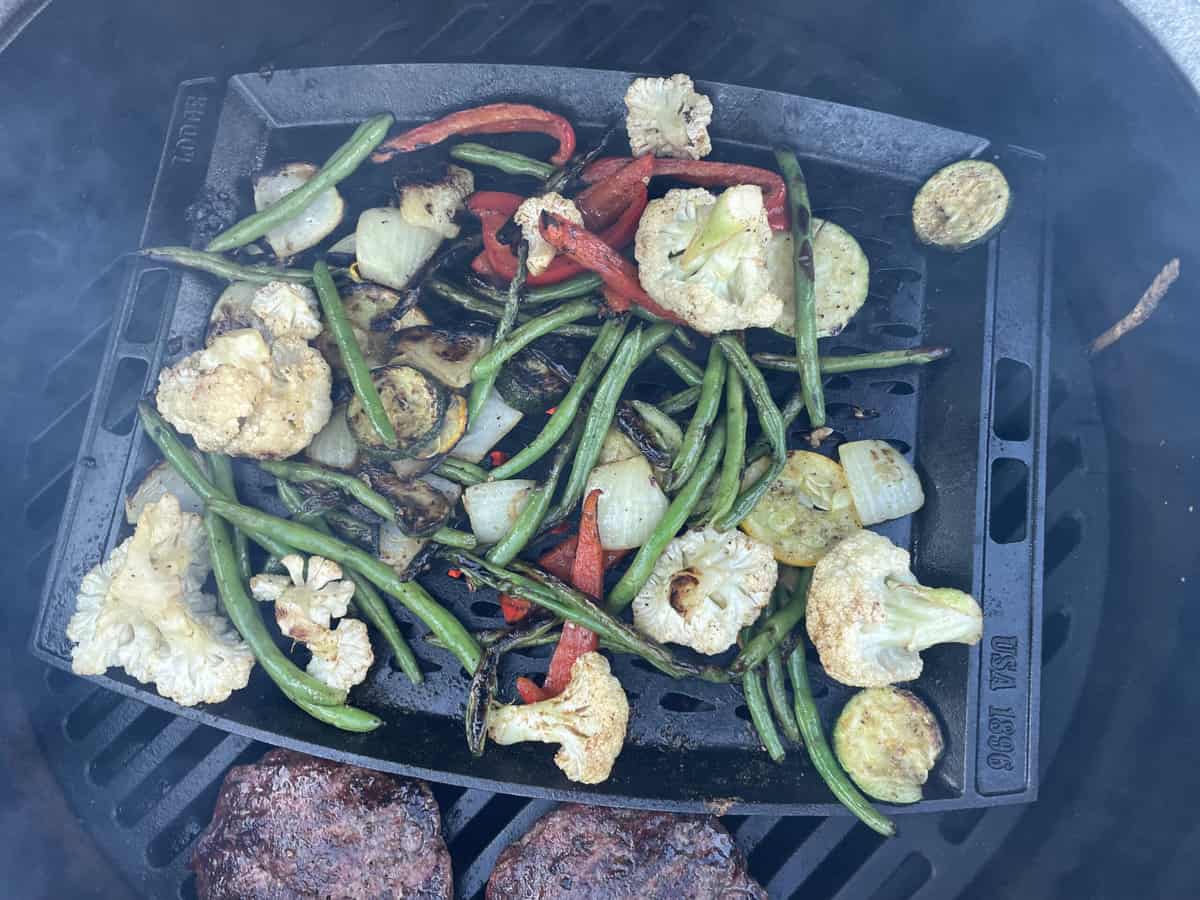 Veggies grilling next to two meat patties