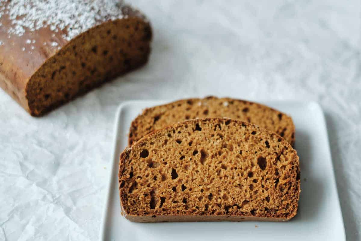 A slice of gingerbread loaf on a pate on a white surface.