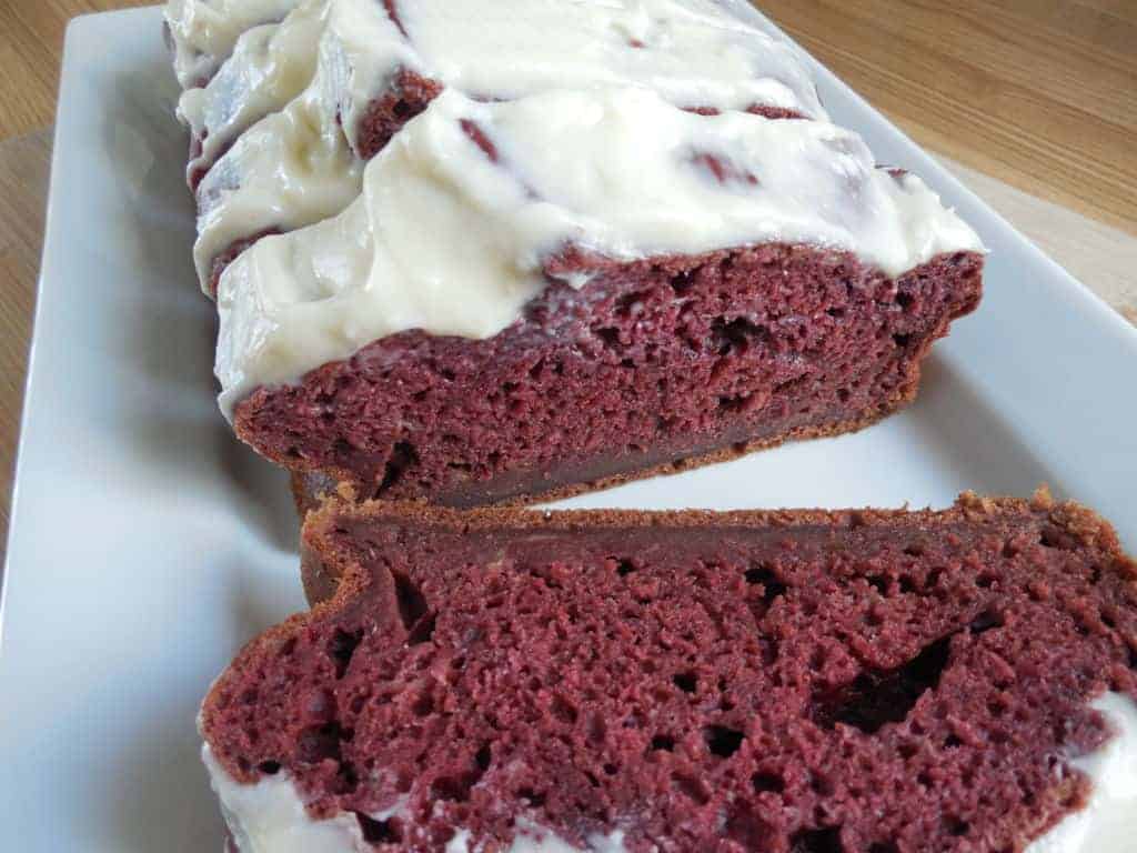 A loaf of red velvet banana bread with cream cheese on a plate on a wooden table.