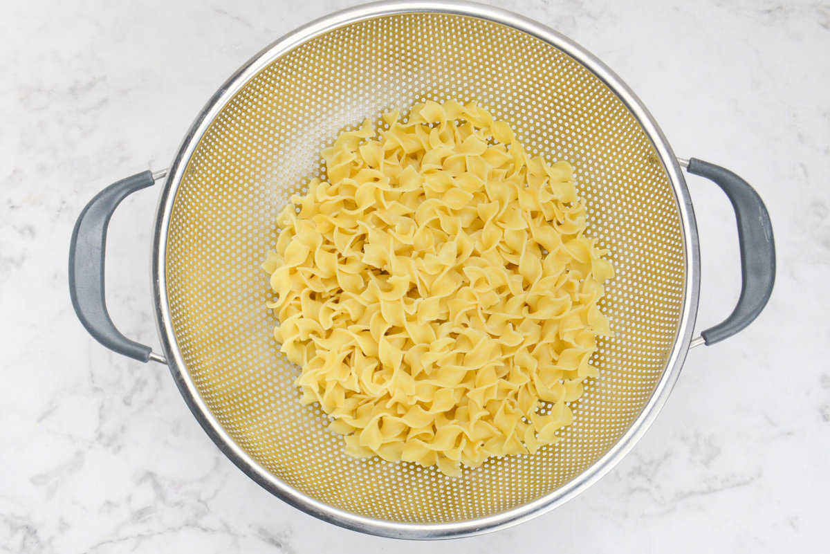 A silver collander with drained yellow noodles 