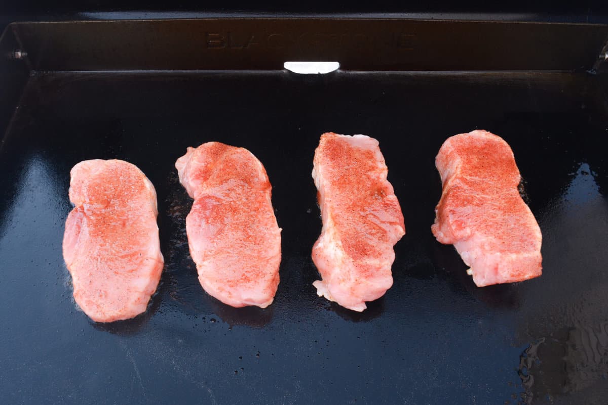 four boneless pork chops cooking on hot blackstone griddle