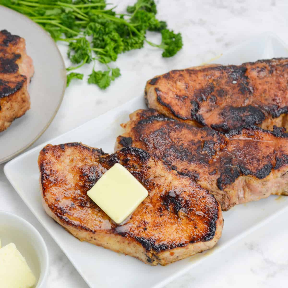 finished blackstone pork chops, plated on a white platter and topped with butter