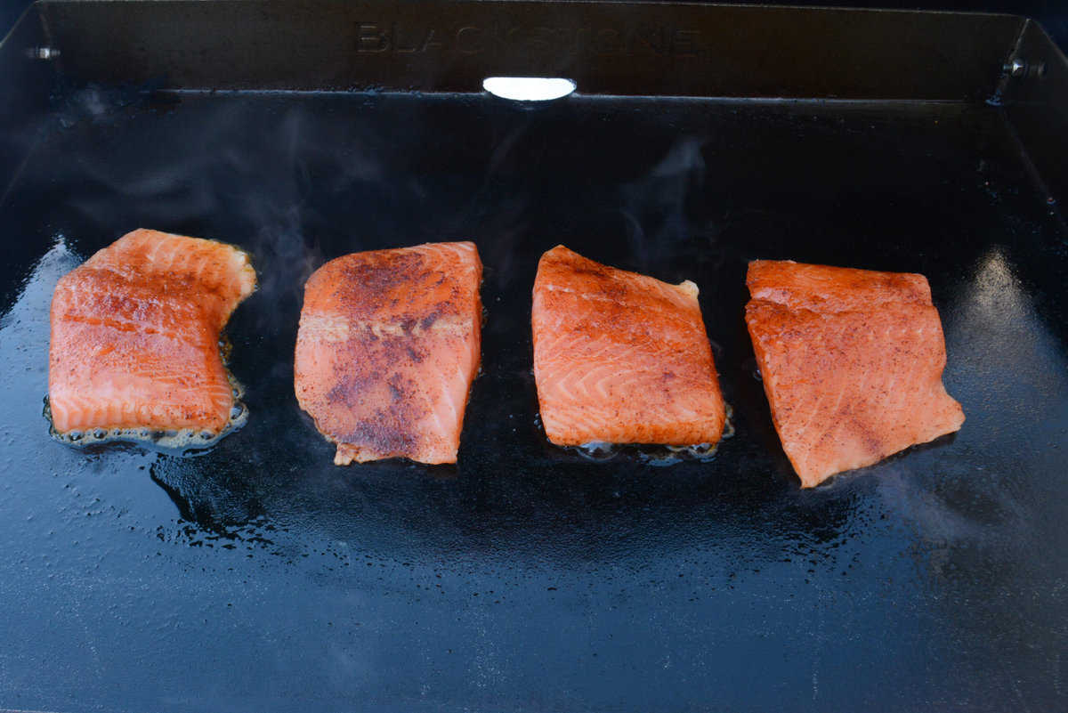 four salmon filets sitting on a hot blackstone griddle