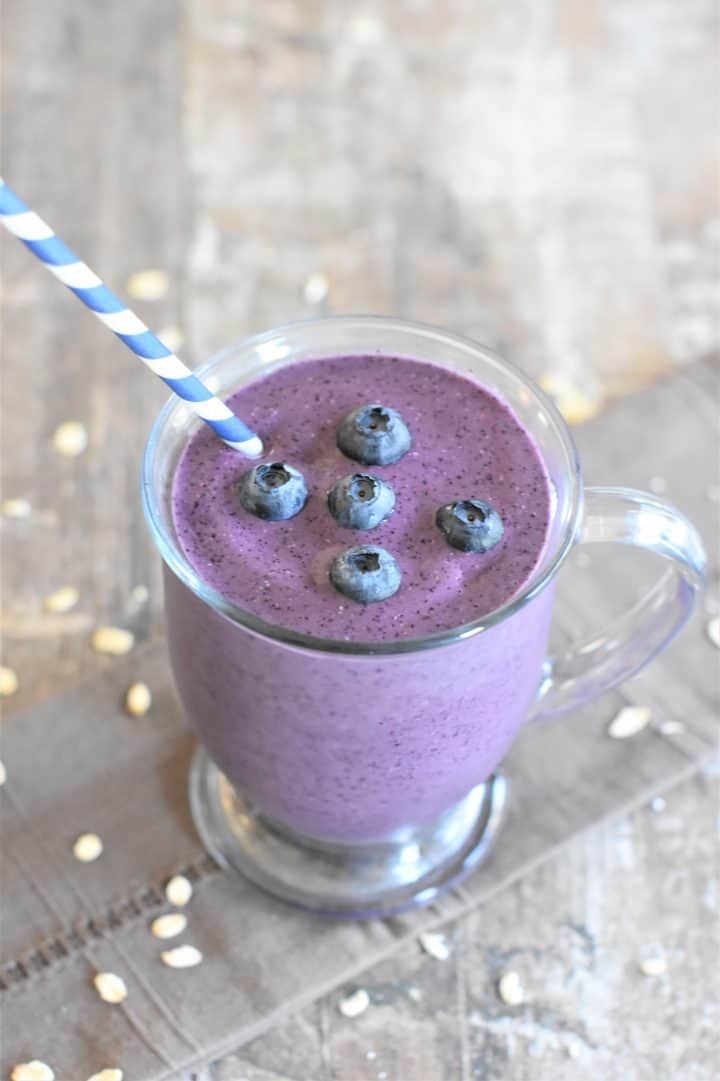 Blueberry pie smoothie in a glass with a straw in it on a table.