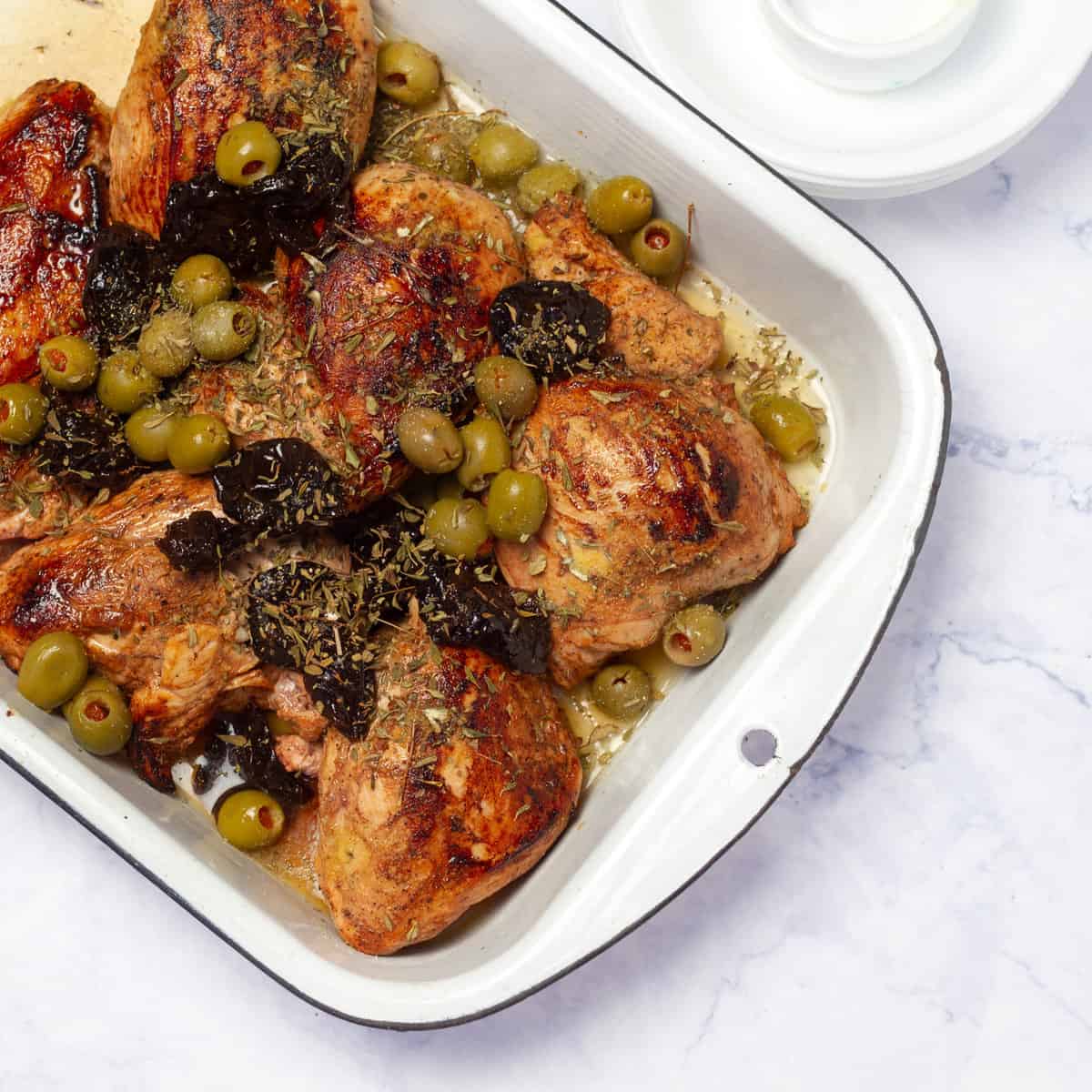 Scatter green olives and pitted prunes around the chicken in the baking dish