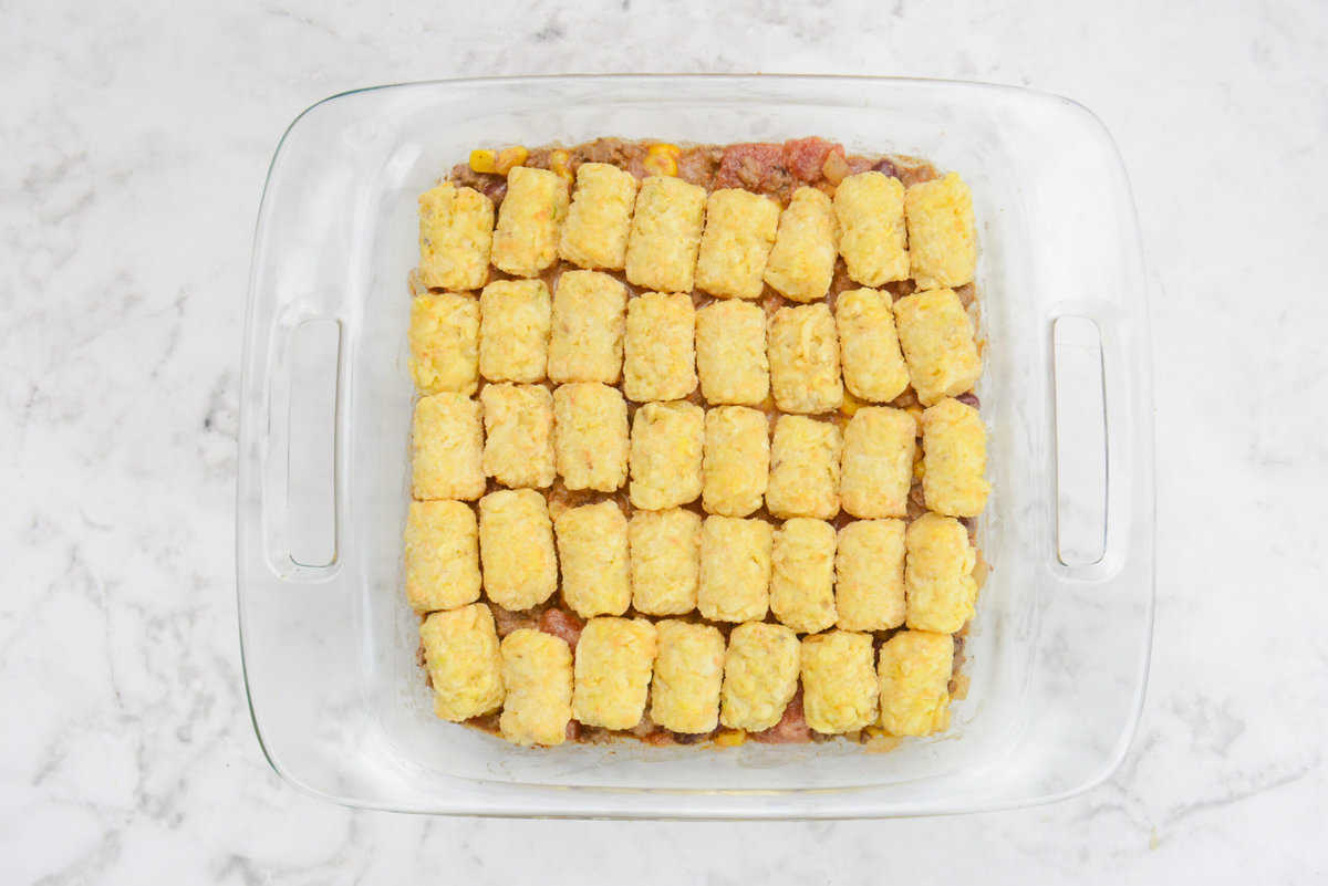 A square casserole dish is shown filled with rows of tater tots topping the dish.