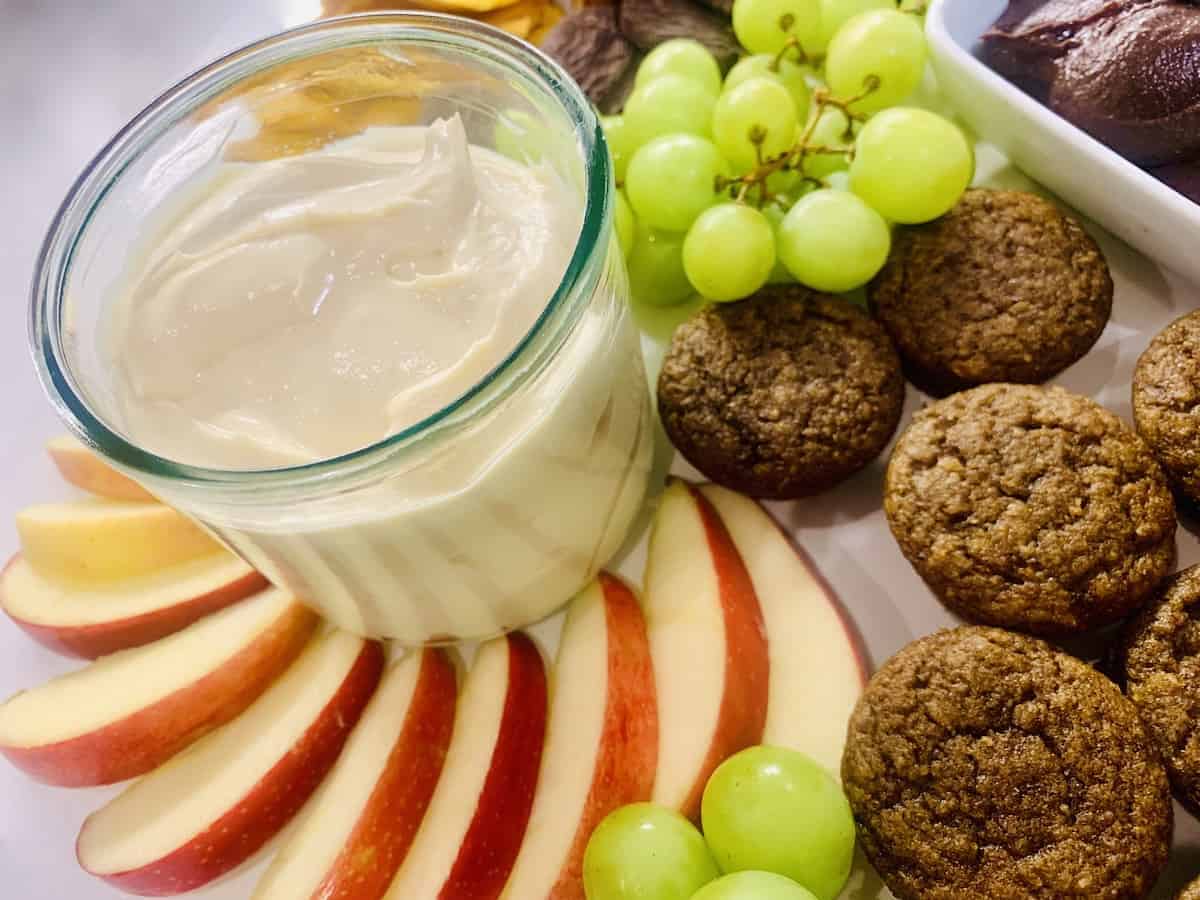 Cream cheese caramel apple dip on a plate with fruit and cookies.