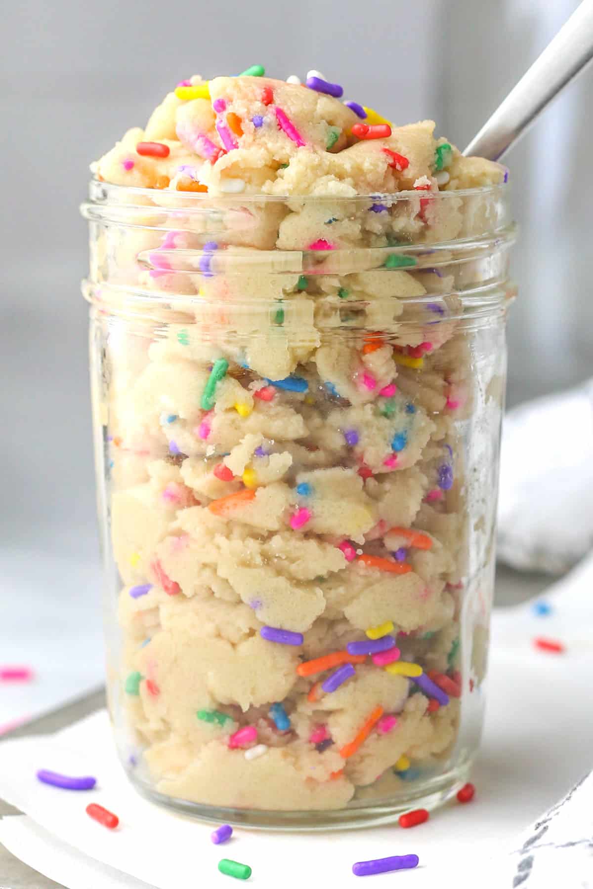 Edible sugar cookie dough in a glass jar with a spoon in it.