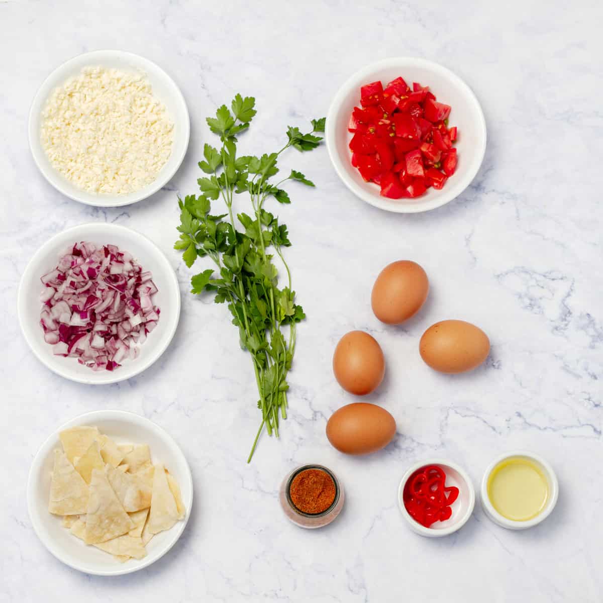 Migas Tex Mex Breakfast ingredients, incuding eggs, tortilla crumbs, tomatoes, onion, cilantro, cheese, and Tex-Mex spices. 