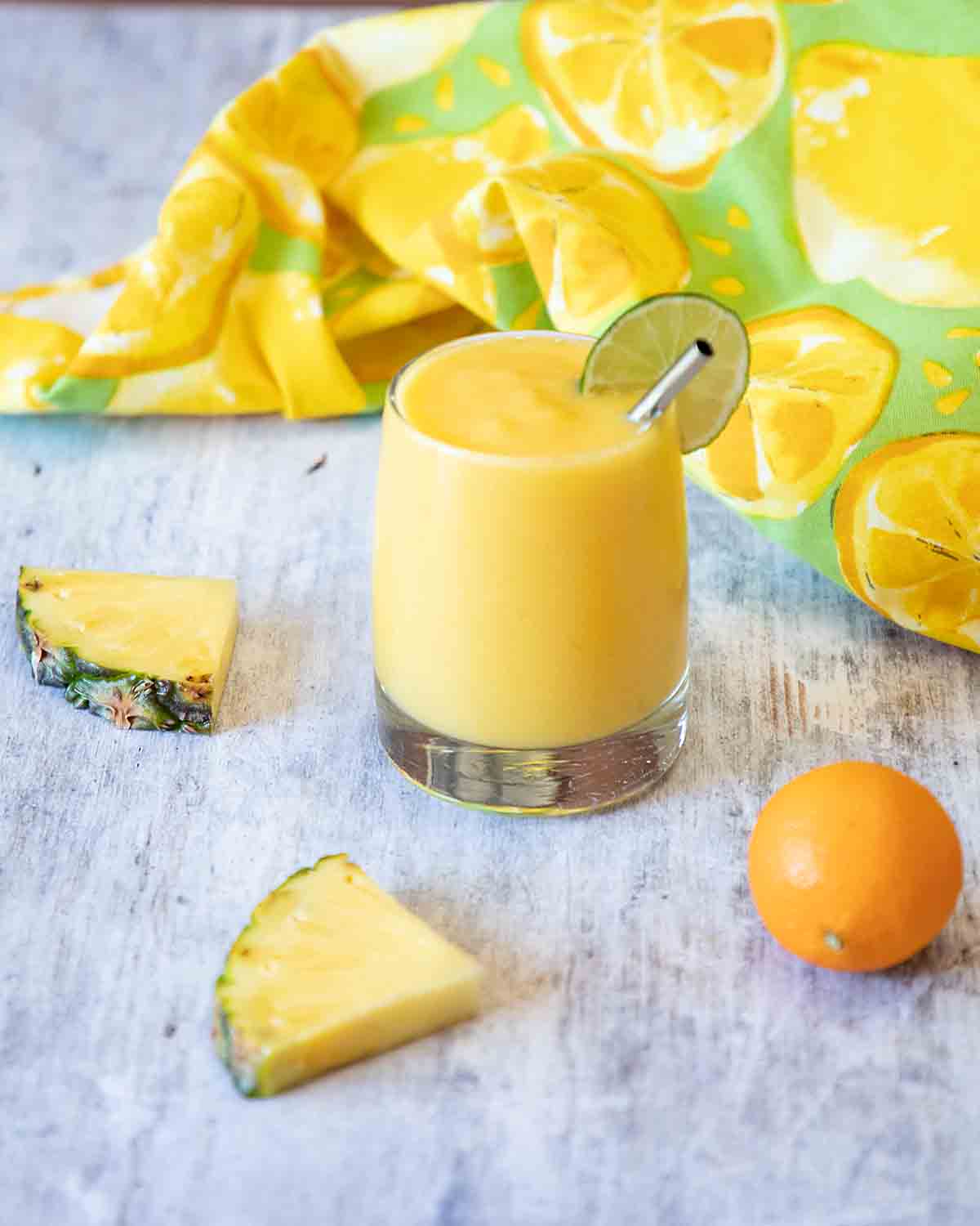 Mango pineapple smoothie in a glass surrounded by fruit.