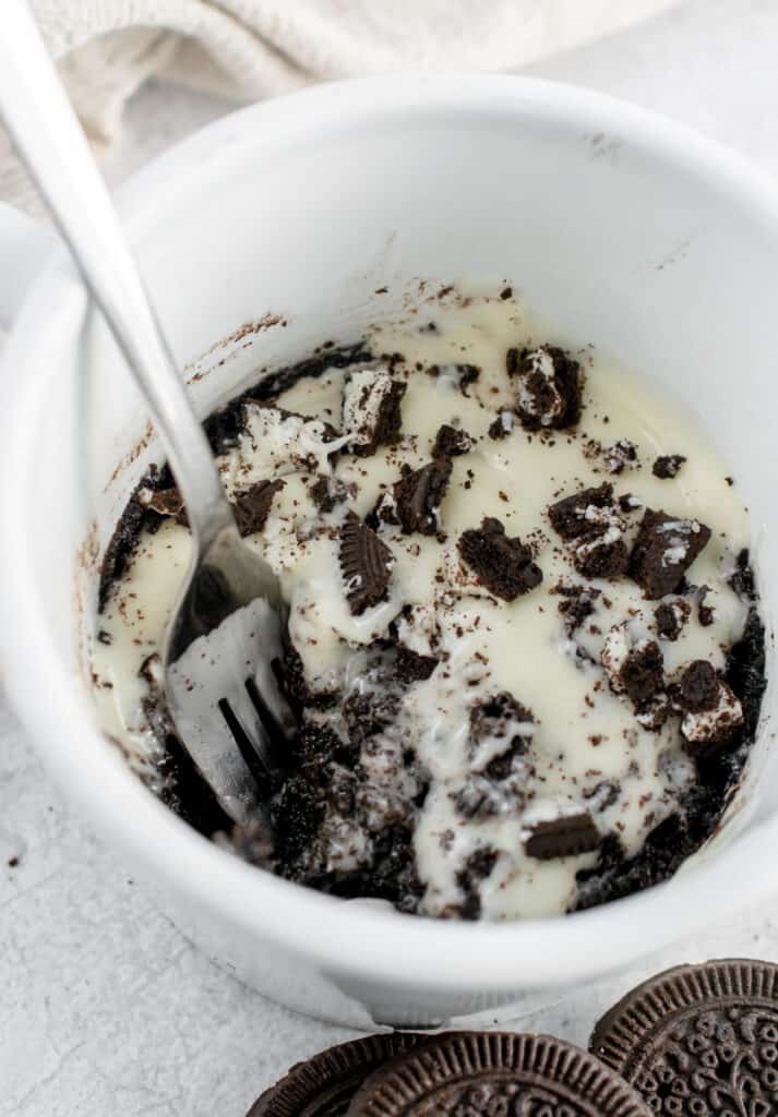 Oreo Mug Cake with a fork in it with cookies around it.