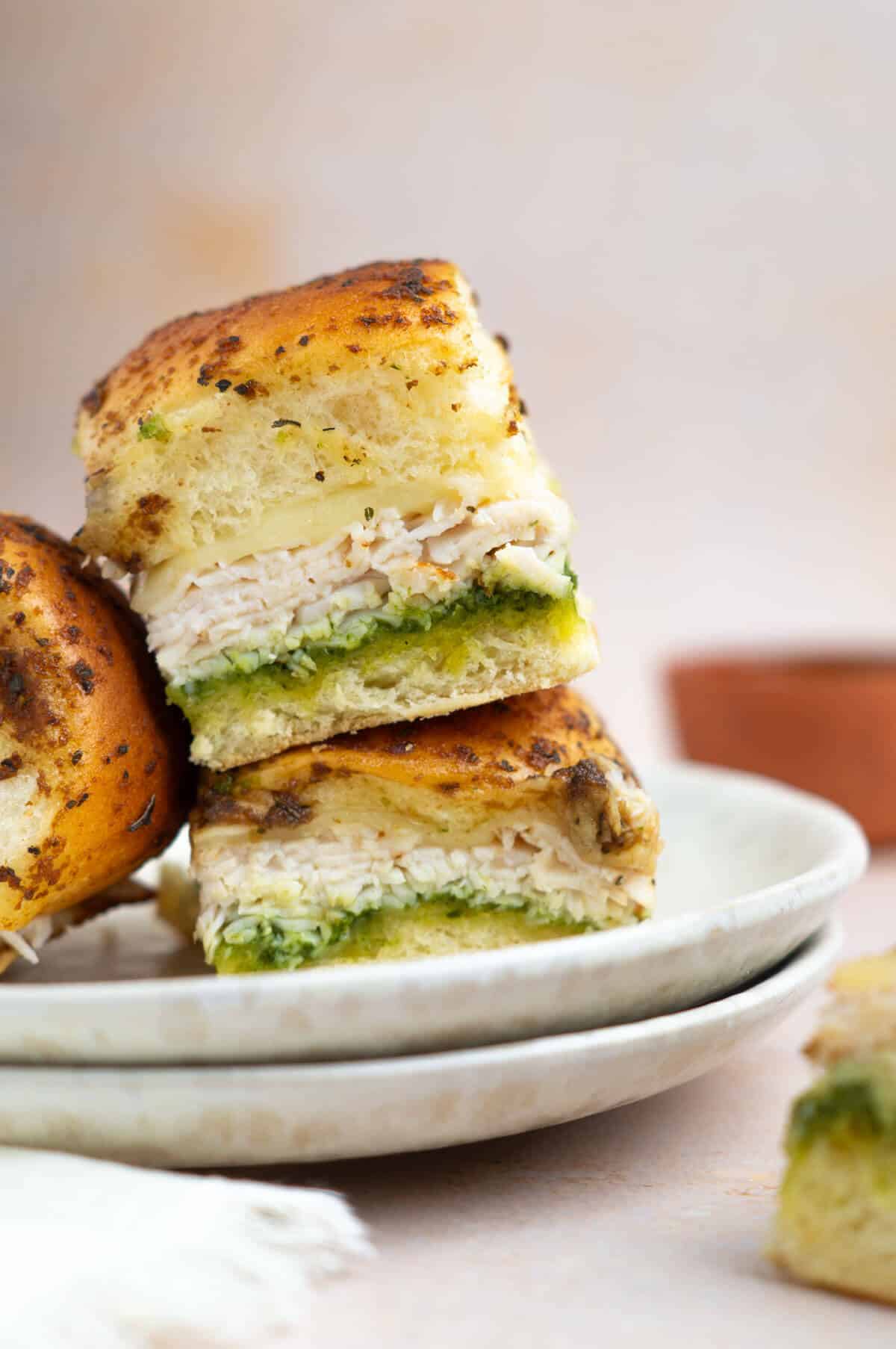 Pesto chicken sliders on white plates on a table.