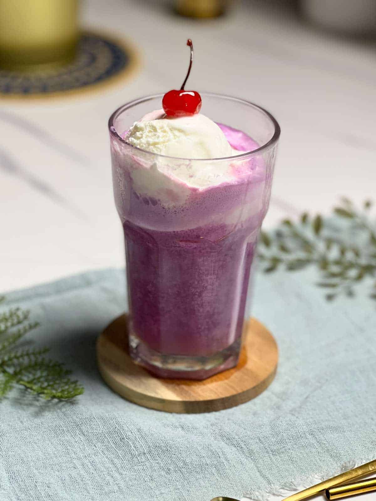 A purple cow float in a glass on a table.