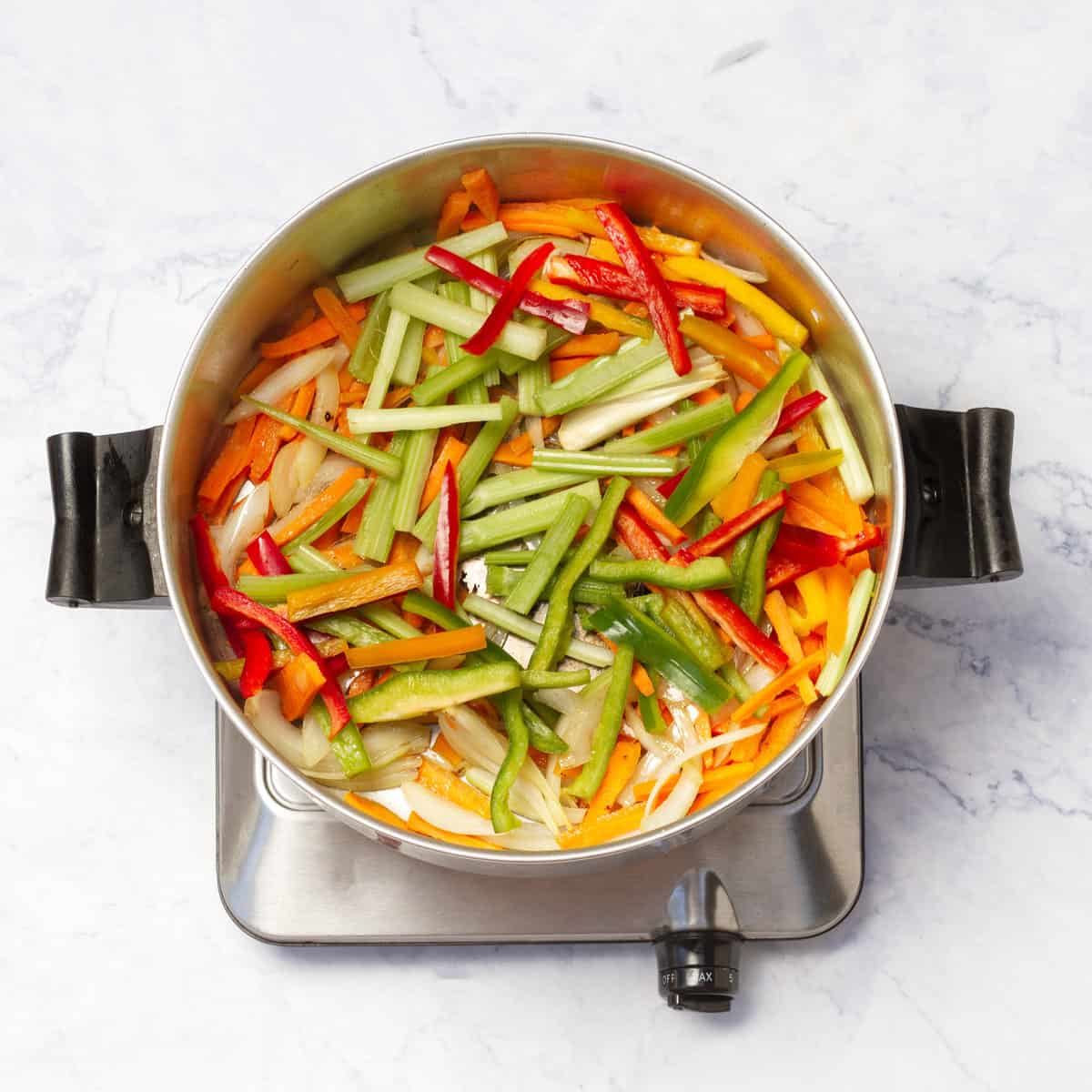 cooking onion, carrot, bell peppers, and celery in a skillet