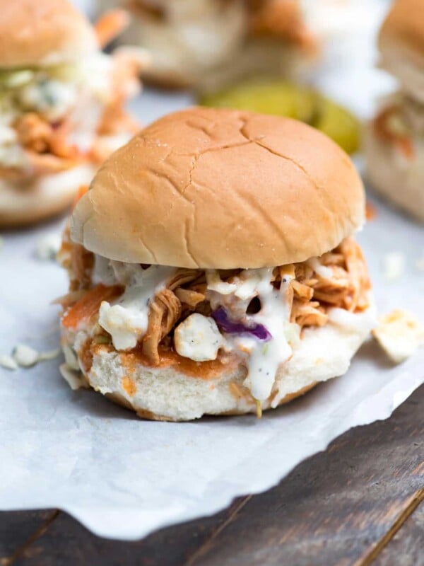 Slow cooker BBQ Buffalo chicken sliders on wax paper on a table.