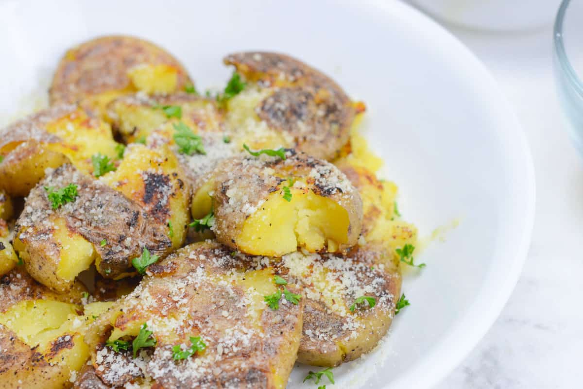 closeup on blackstone smashed potatoes, coated in grated parmesan cheese and sprinkled with parsley. 