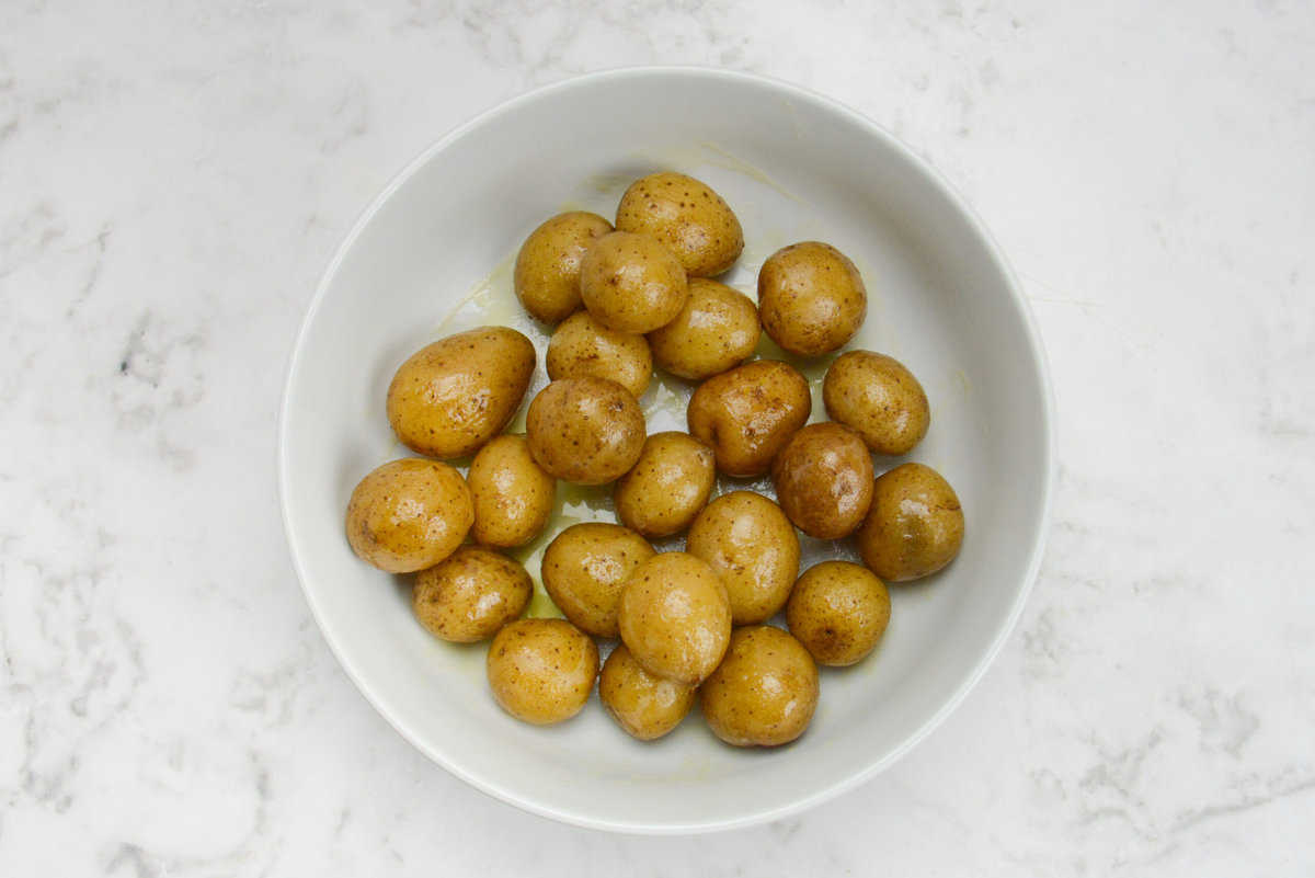baby potatoes covered in olive oil and butter, sitting in a white bowl