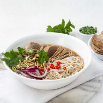 A bowls of cooked rice noodles, thinly sliced beef in the hot broth