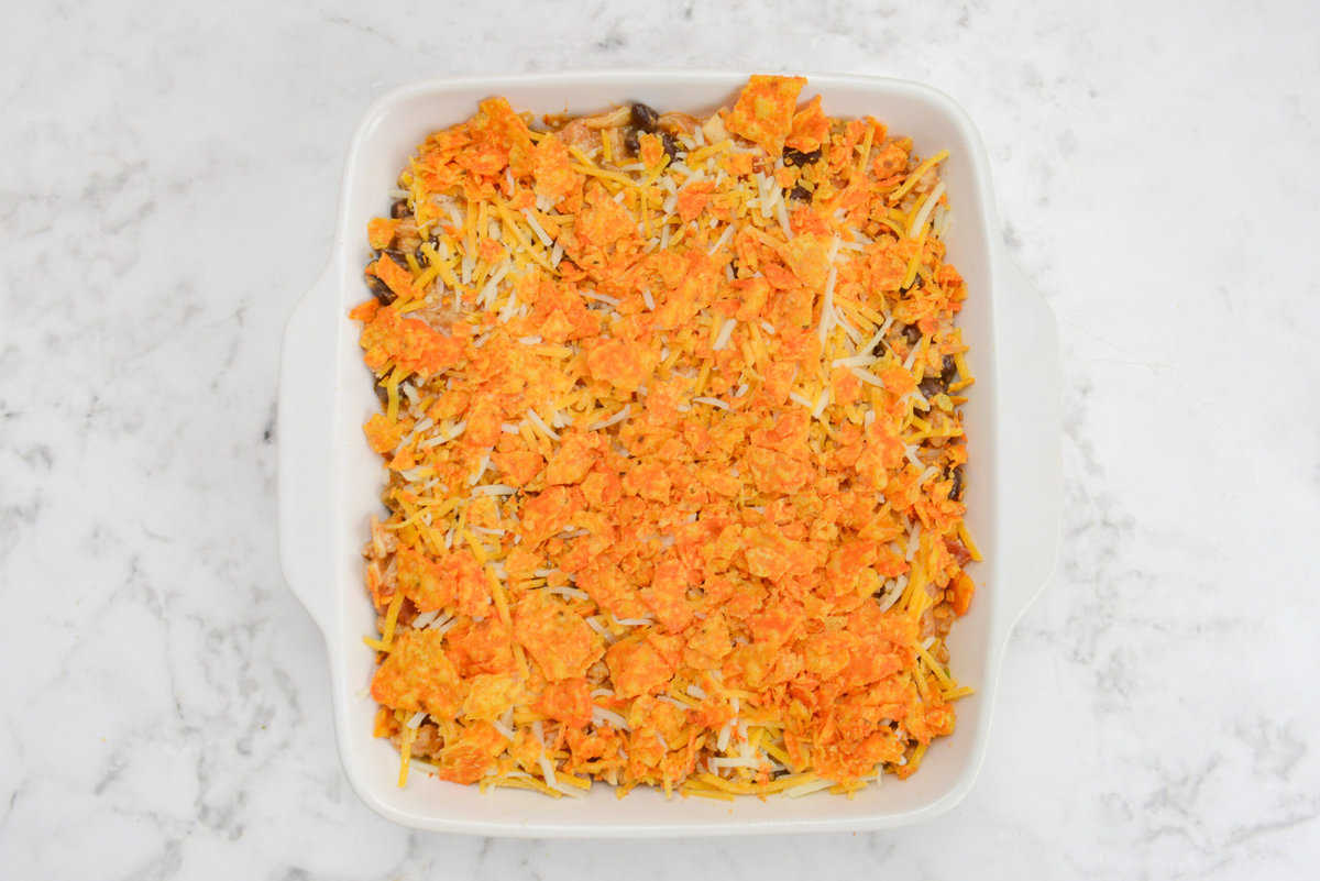 A white square baking dish filled with casserole mixture is topped with bright orange Doritos pieces