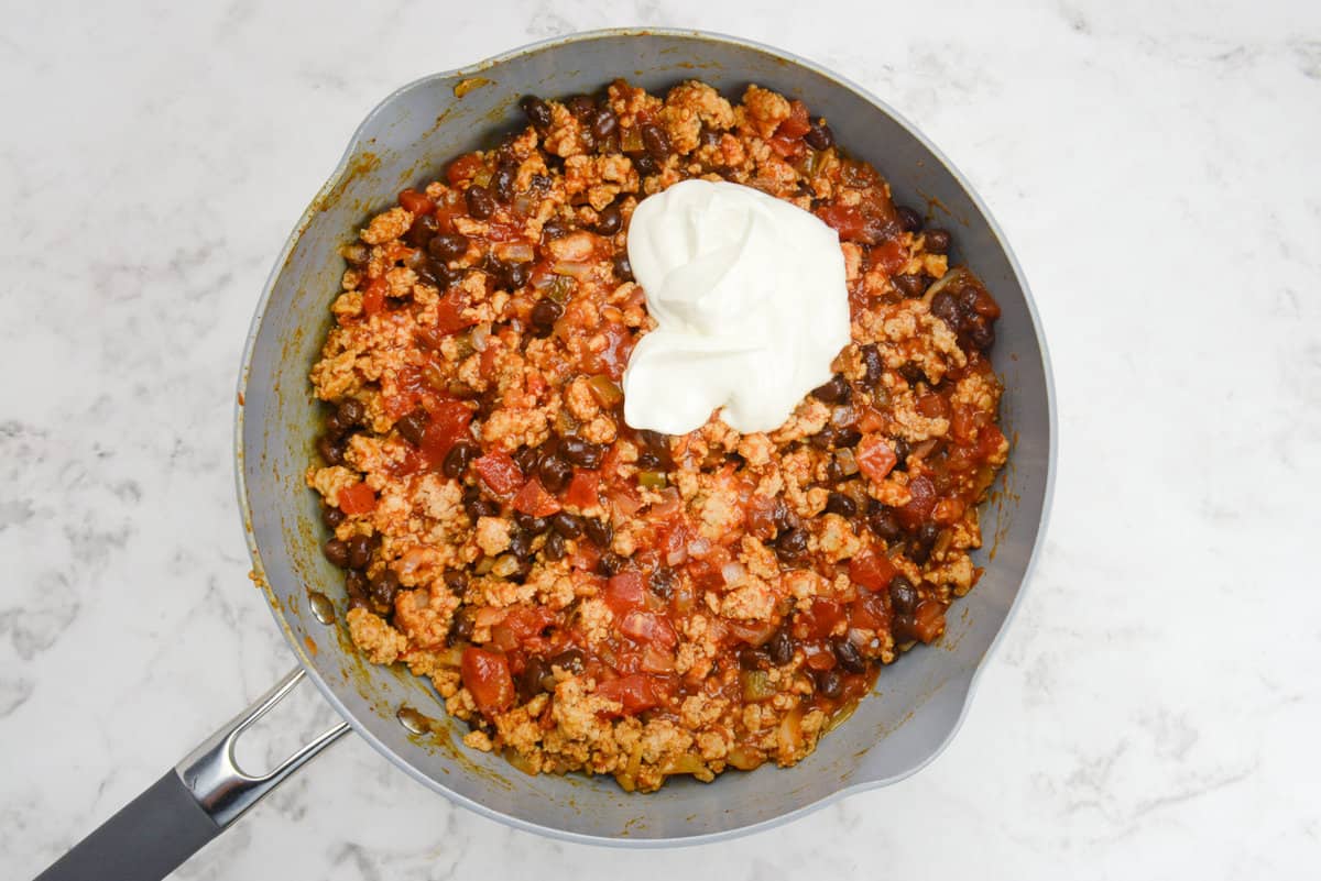 A skillet with casserole filling and a scoop of Greek yogurt