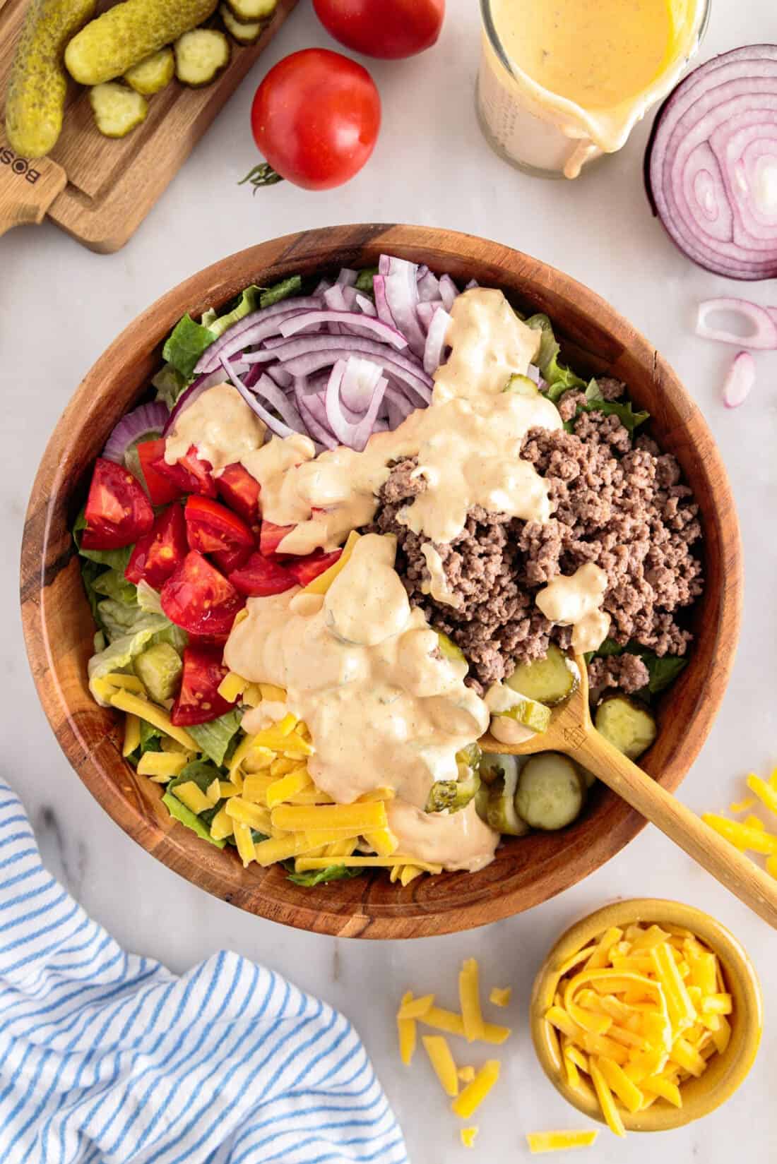 A Big Mac Salad in a wooden bowl on a table with ingredients on it.