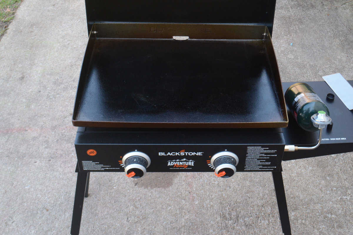 A Blackstone griddle on a patio with temperature knobs set to medium-low.