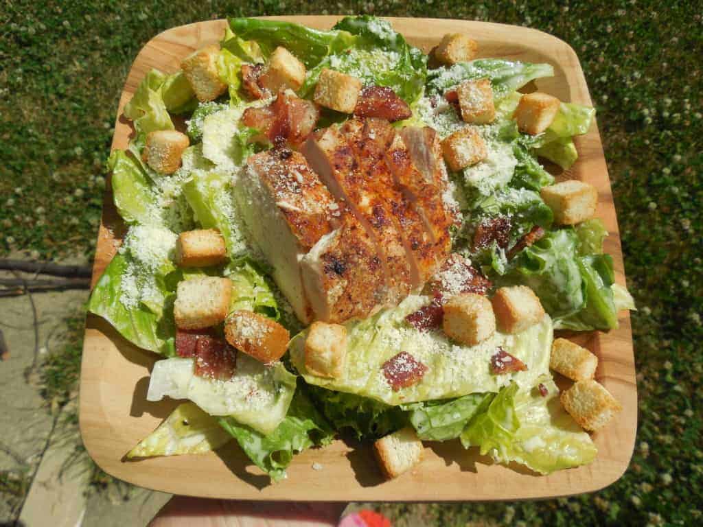 A Chicken Caesar Salad on a wooden tray.