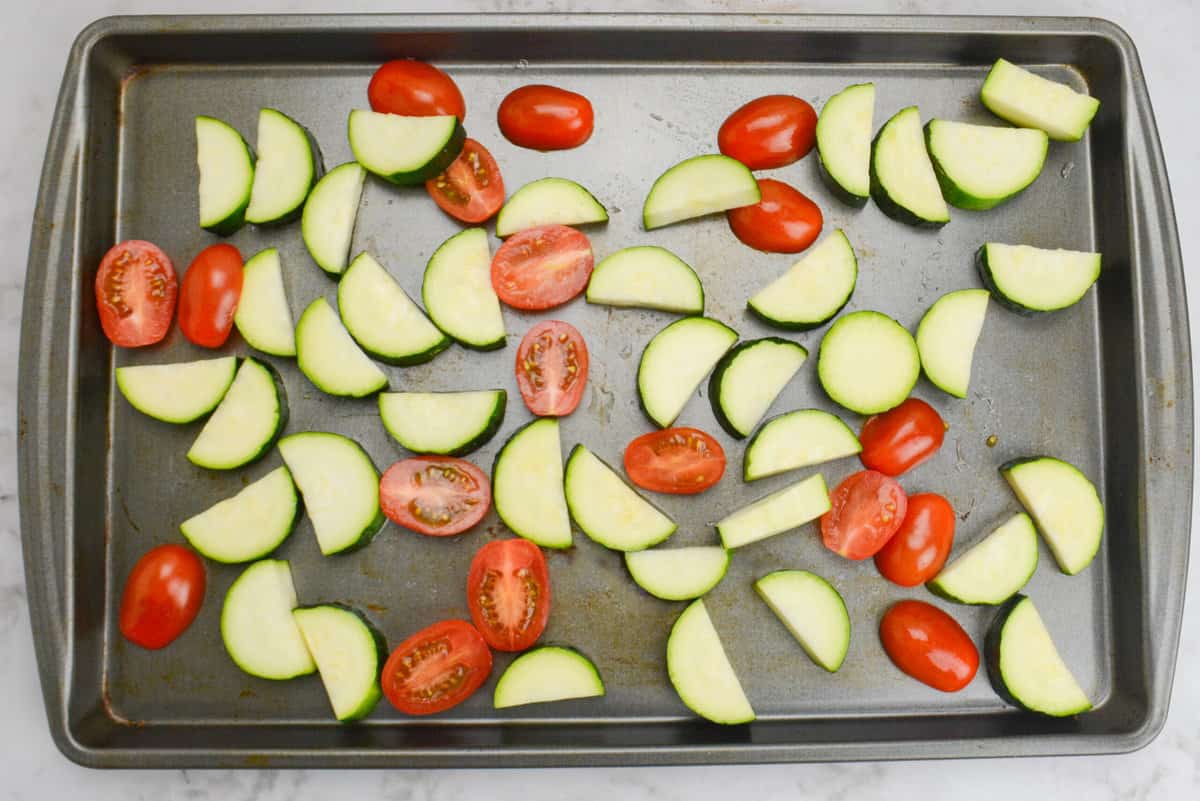 A sheet pan with halved cherry tomatoes and bite half-moon zucchini cuts