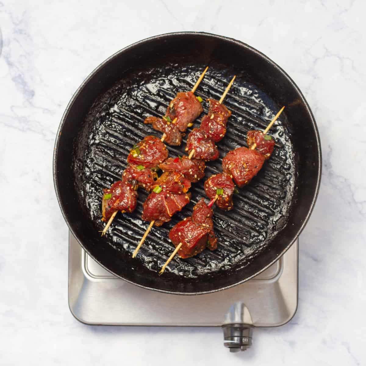 marinated beef cubes thread onto skewers and placed on fry pan