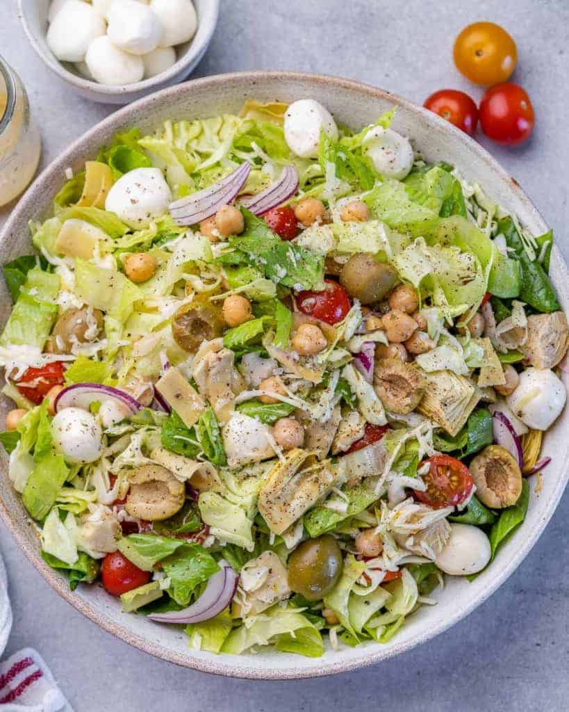An Italian Chopped Salad in a bowl with ingredients around it.