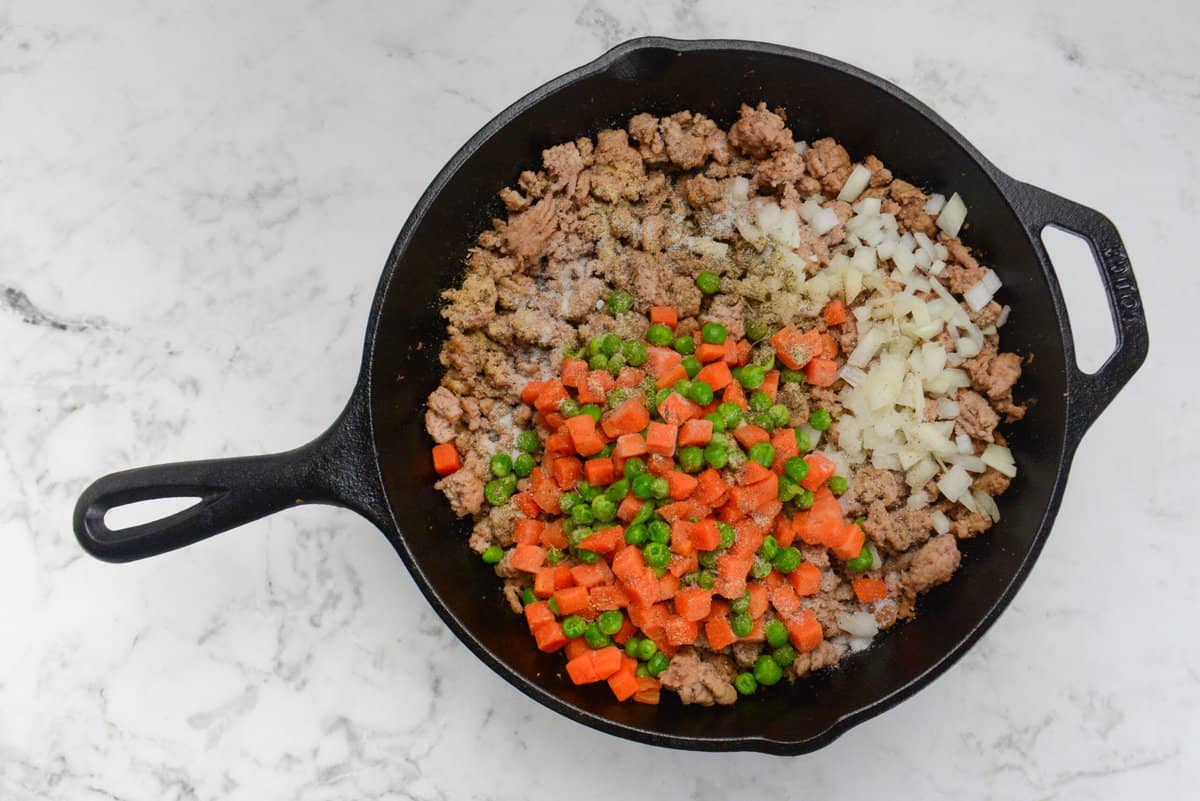 A cast iron skillet with browned ground turkey and topped with vegetables and seasoning