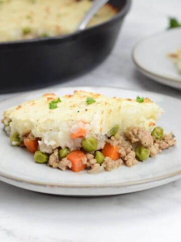 Plate of turkey shepherd's pie sits on a plate. Cast iron skillet and a small plate sit behind