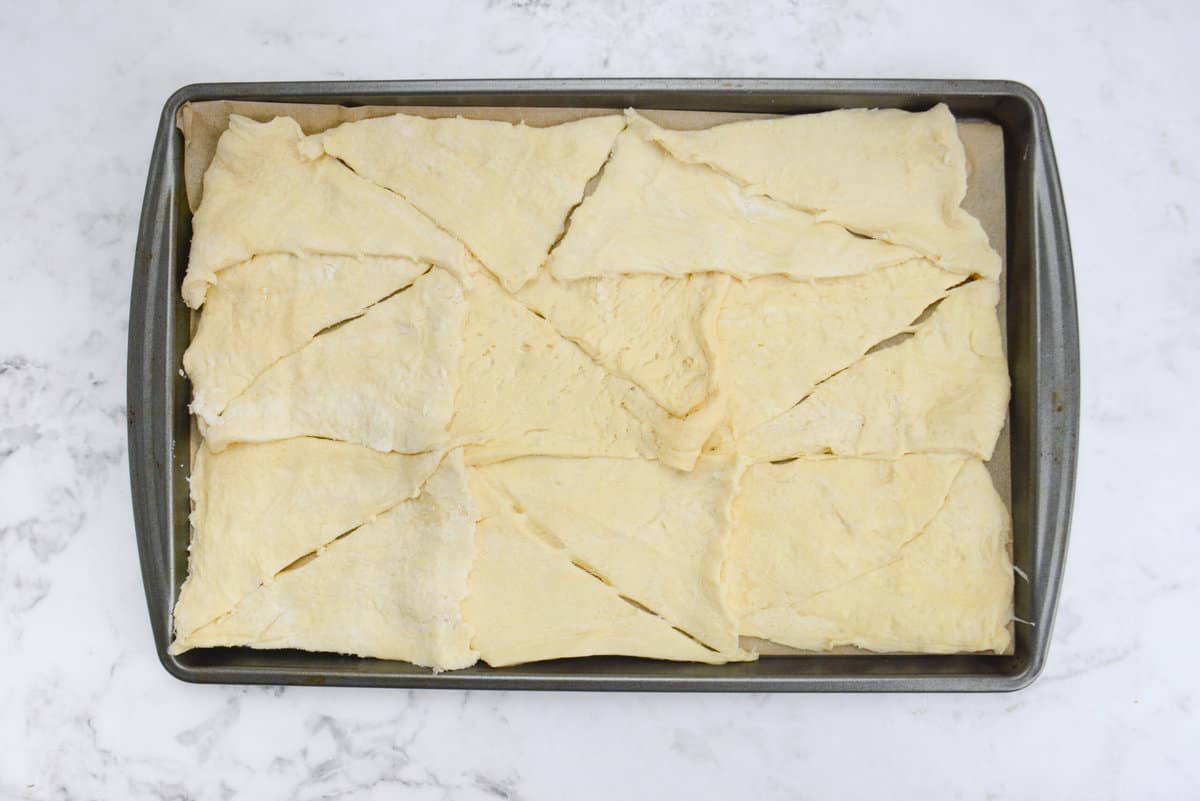 A baking sheet lined with parchment and the uncooked dough. The triangles are still visible and not pressed together.