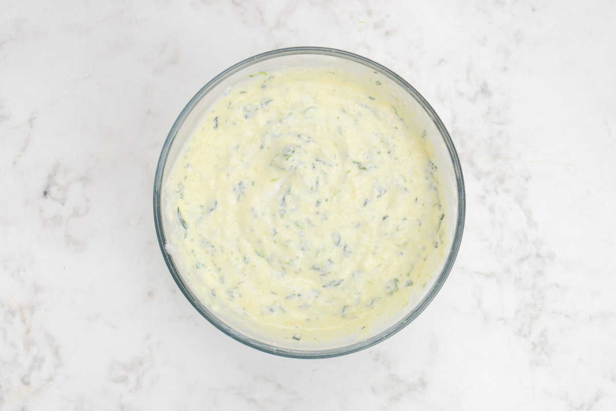 A bowl of the cottage cheese and ricotta mixture tinted slightly yellow with streaks of spinach