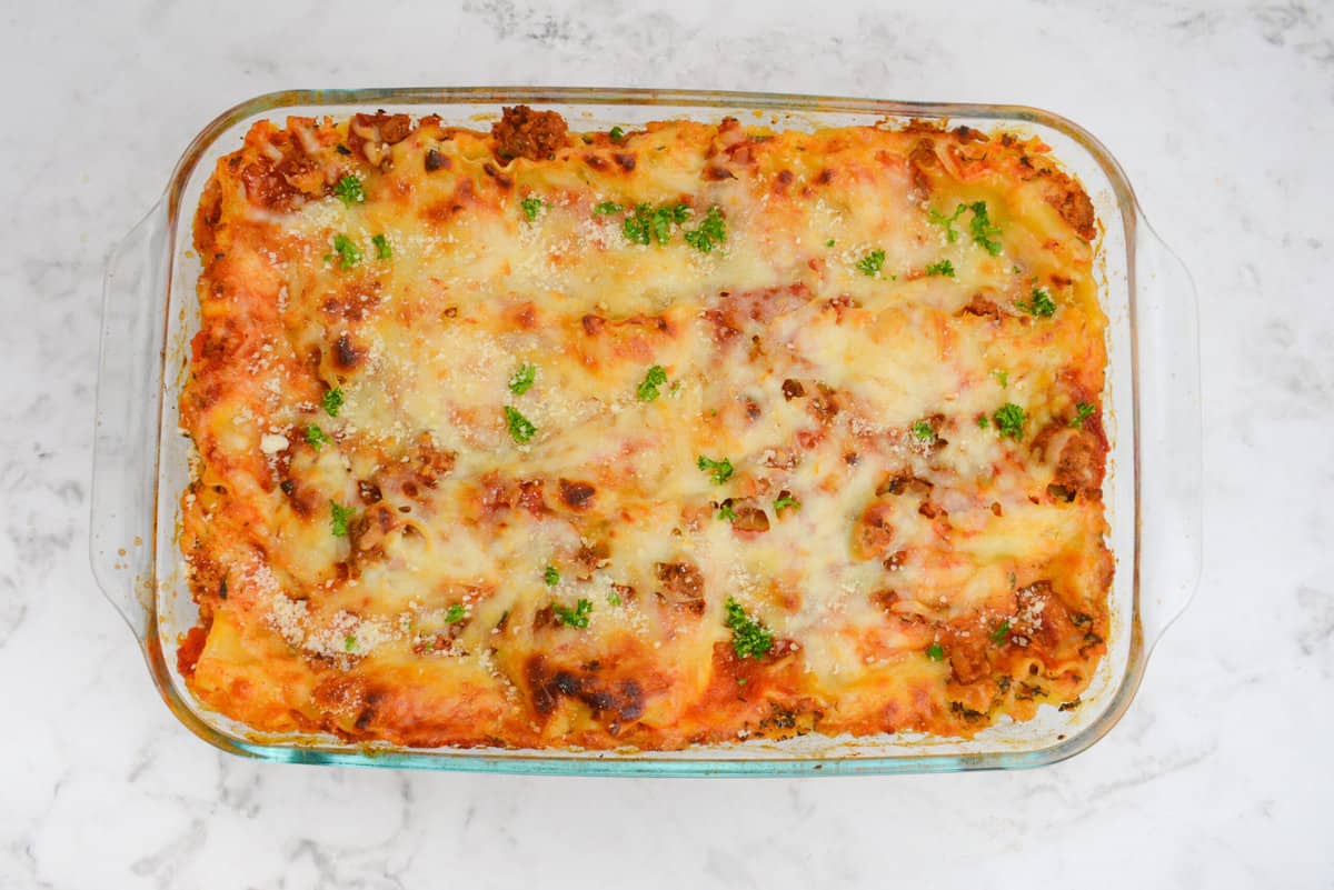 The baked uncut lasagna. Browned on the top and edges and garnished with fresh parsley. 