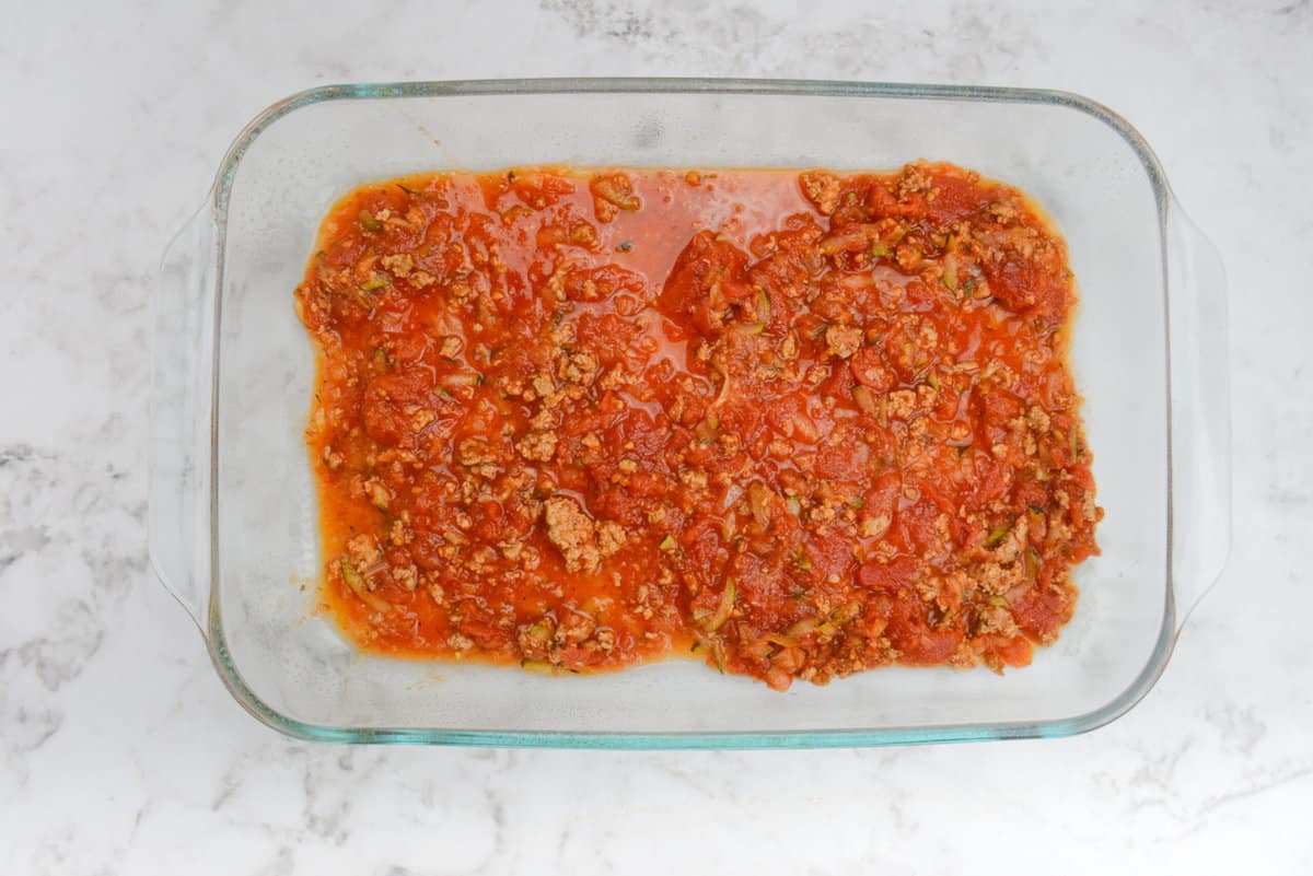A clear baking dish with  the first layer of meat sauce on the bottom