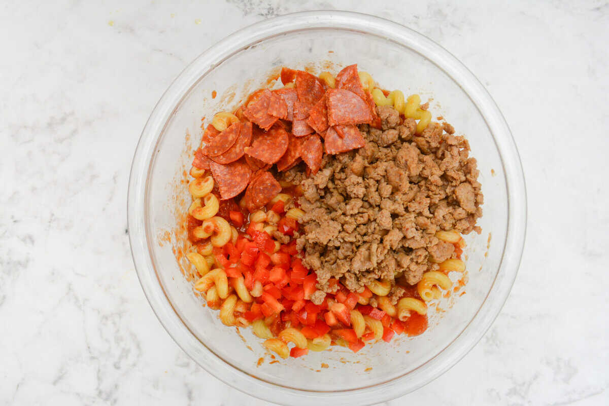 The bowl with the pasta and sauce is now topped with pepperoni, bell pepper and turkey sausage 